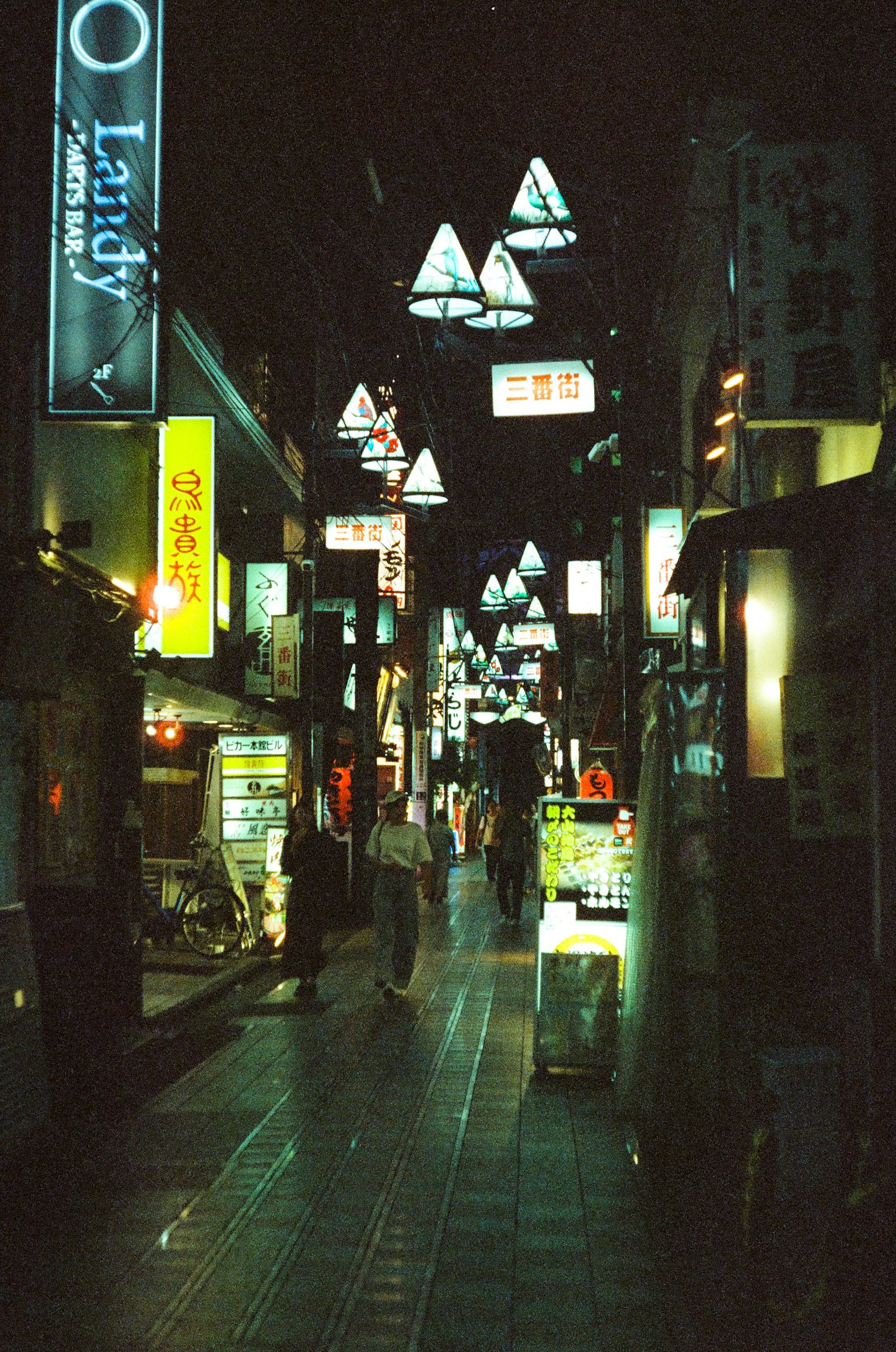 ฉากถนนยามค่ำคืนที่มีไฟสามเหลี่ยมและป้ายไฟนีออนส่องสว่างในซอย