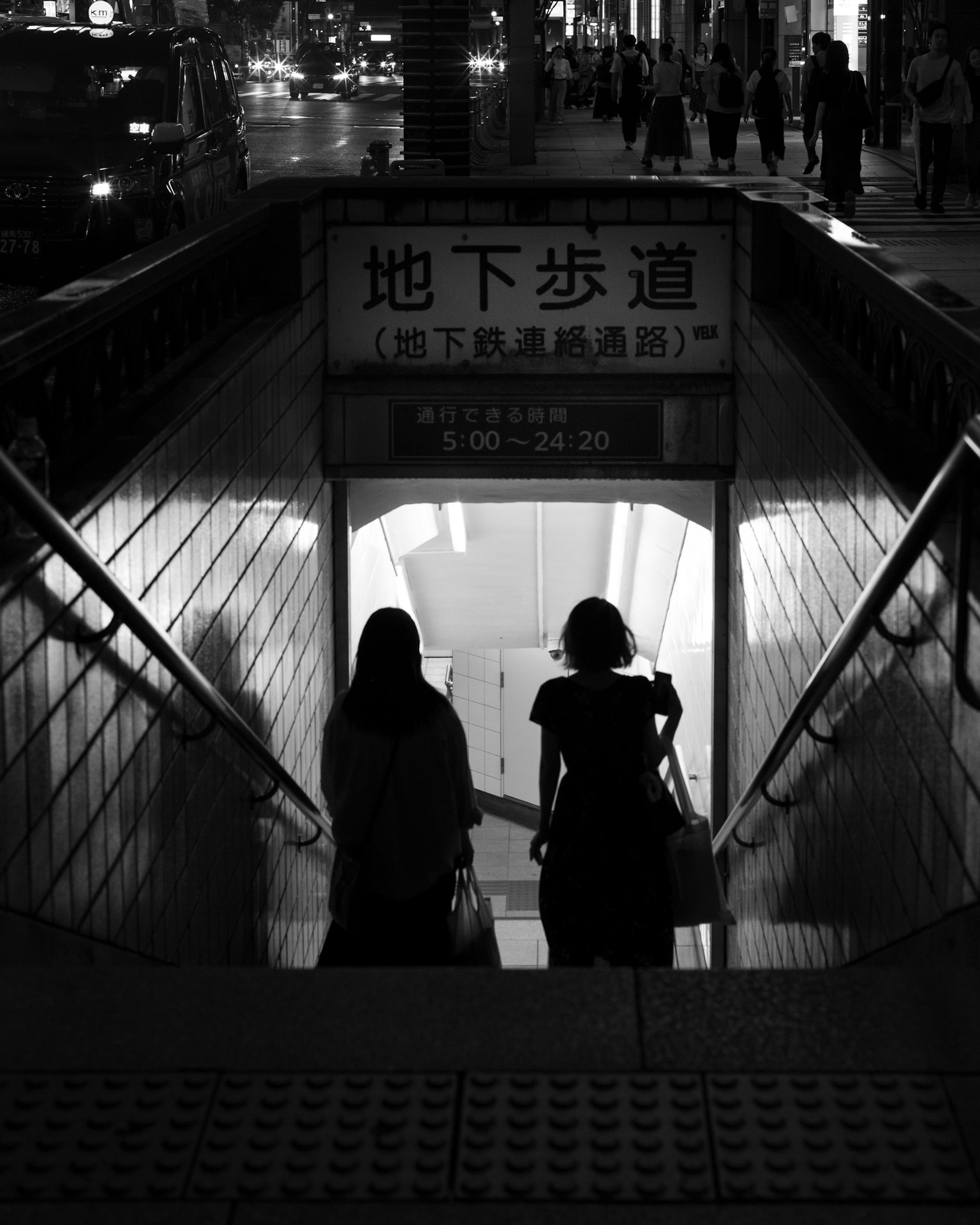 Siluetas de dos mujeres bajando escaleras en la entrada de un paso subterráneo