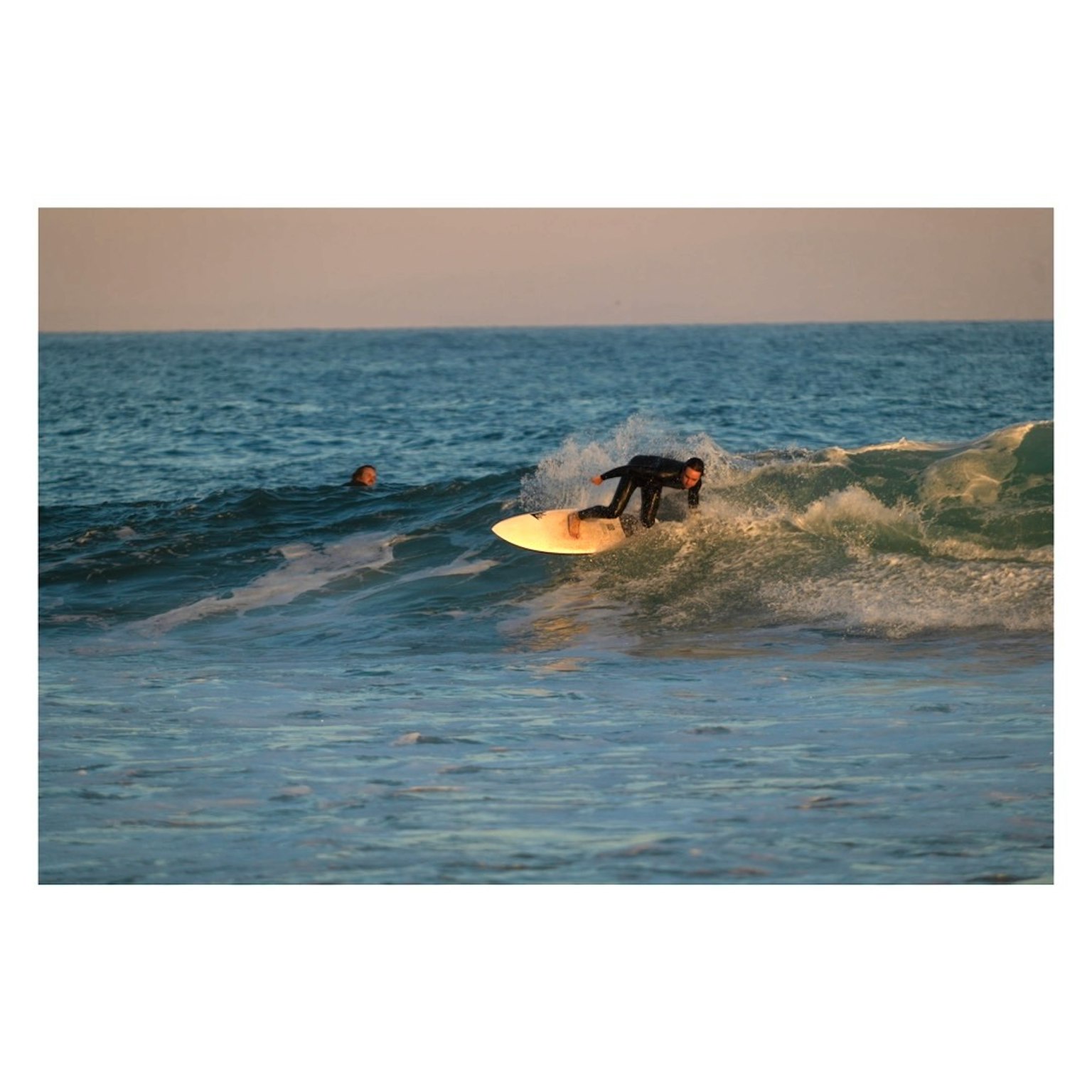 Un uomo che fa surf su un'onda con un altro surfista sullo sfondo