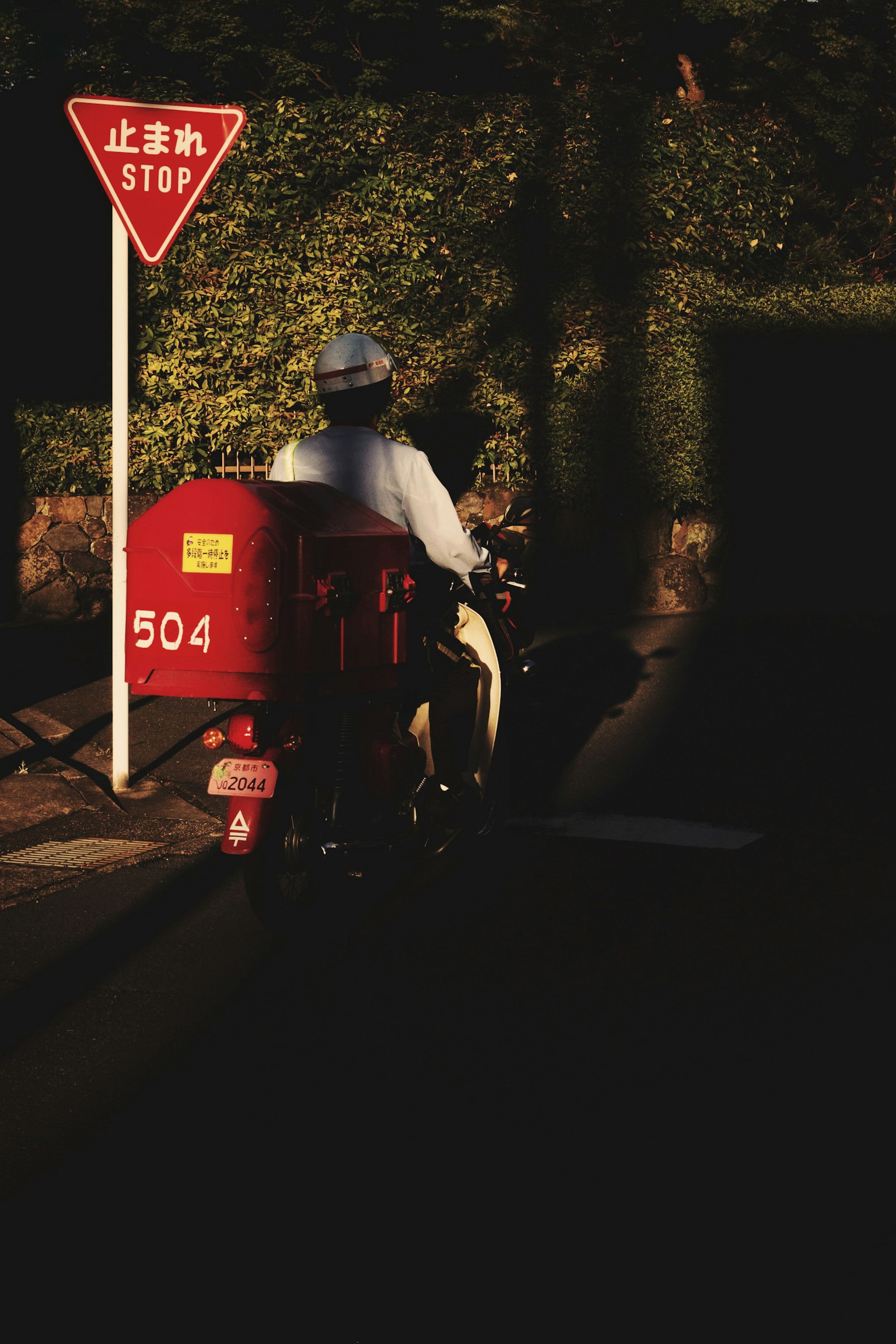 Delivery person on a red motorcycle passing by a stop sign