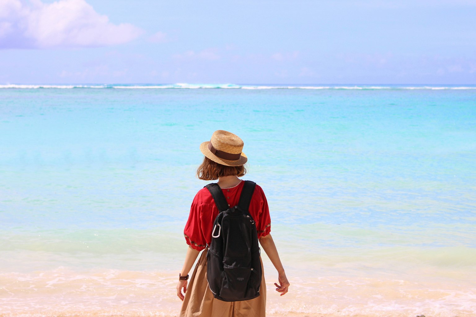 Woman standing on the beach looking at the sea wearing a red top and straw hat