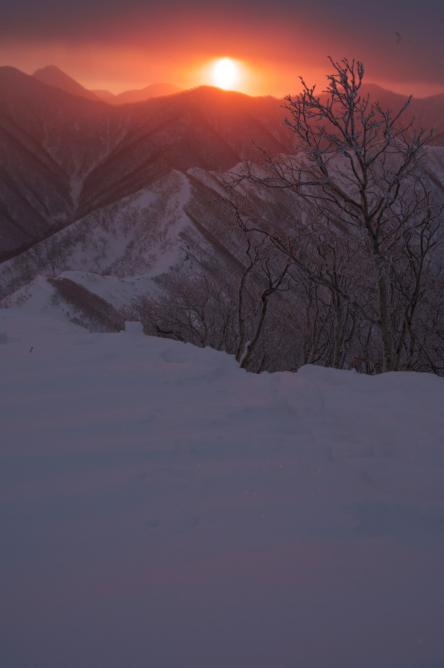 Bellissima vista del tramonto con il sole che sorge tra le montagne coperte di neve