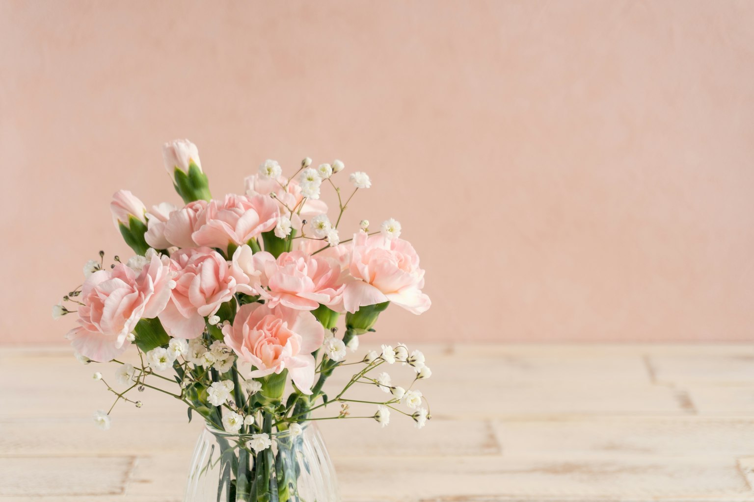 Un vaso con garofani rosa e fiorellini di gipsophila su uno sfondo rosa chiaro