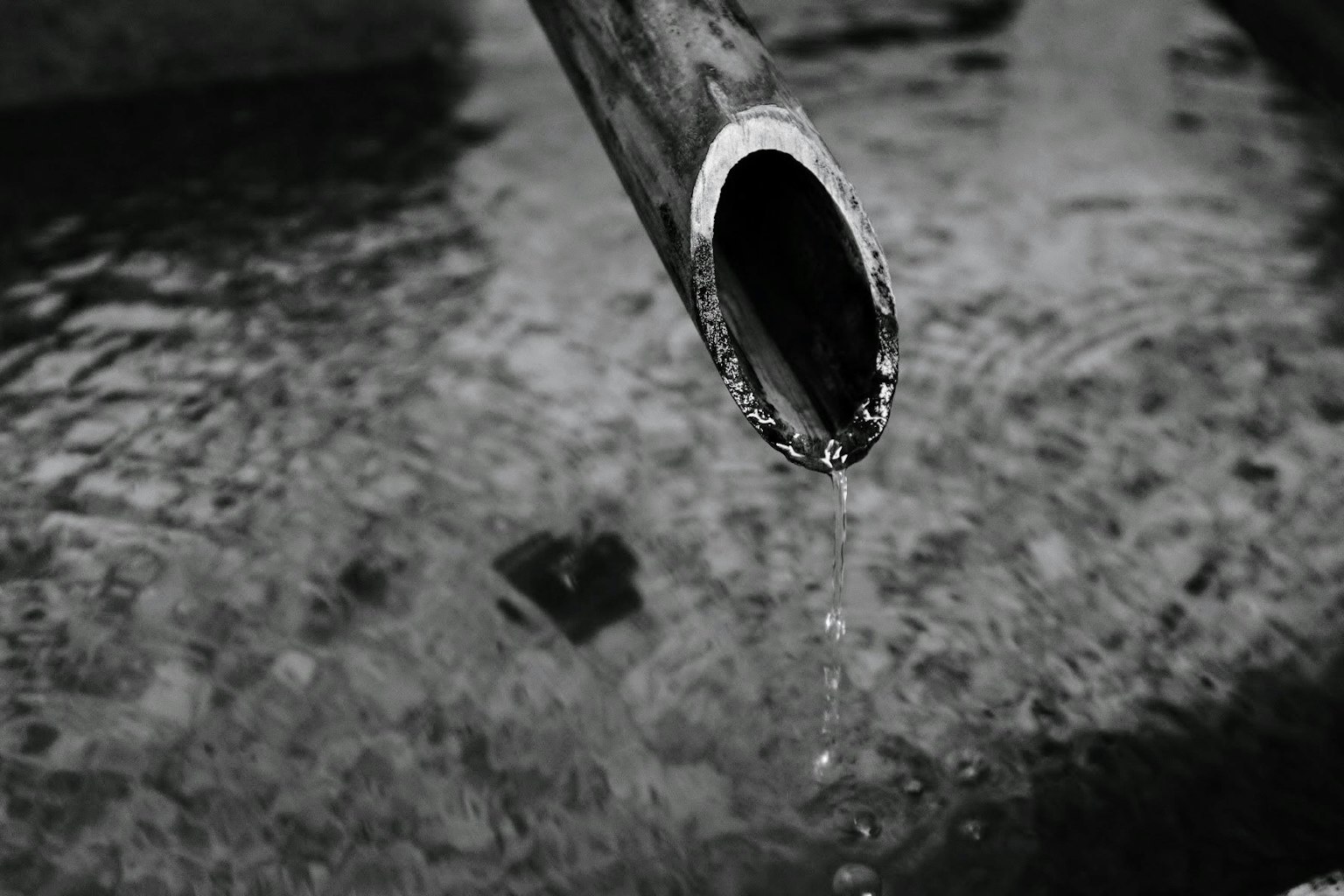 Primo piano di un tubo di metallo che gocciola acqua su una superficie increspata in bianco e nero