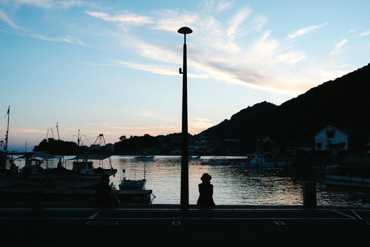 Silhouette of a person by the harbor at dusk with calm water