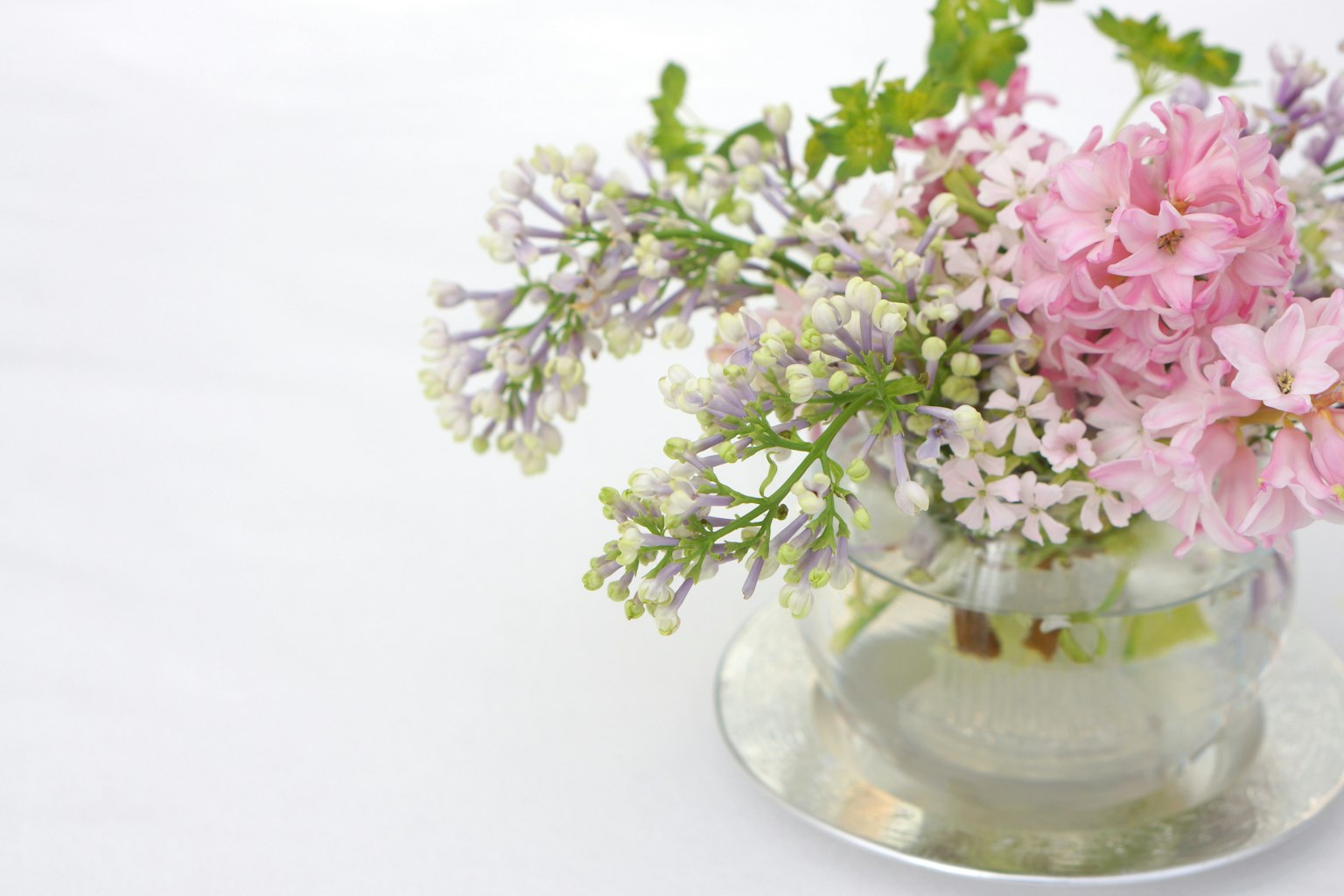 A bouquet of pink and white flowers with green leaves in a clear vase