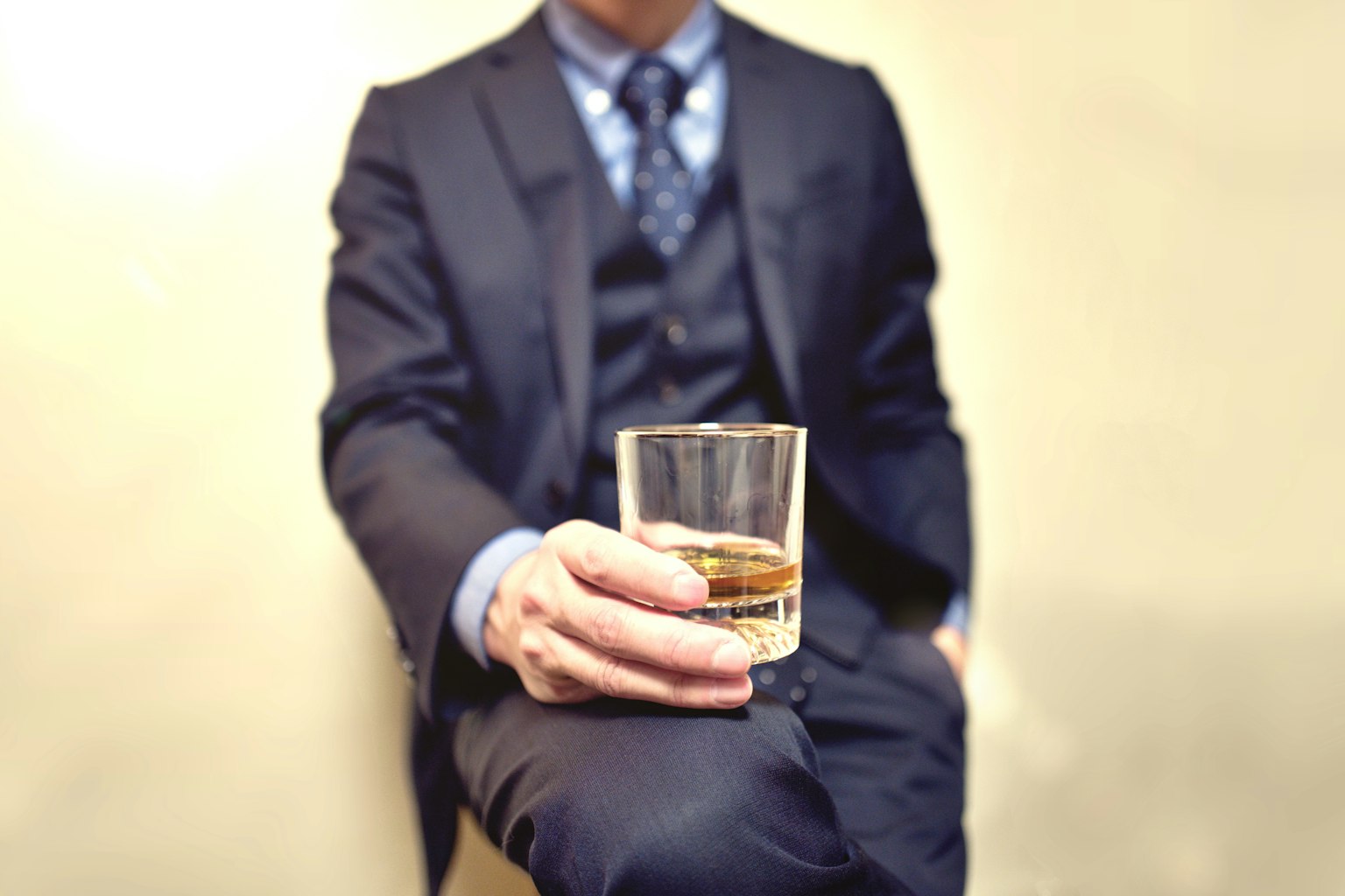 Một người đàn ông trong bộ suit cầm ly whisky