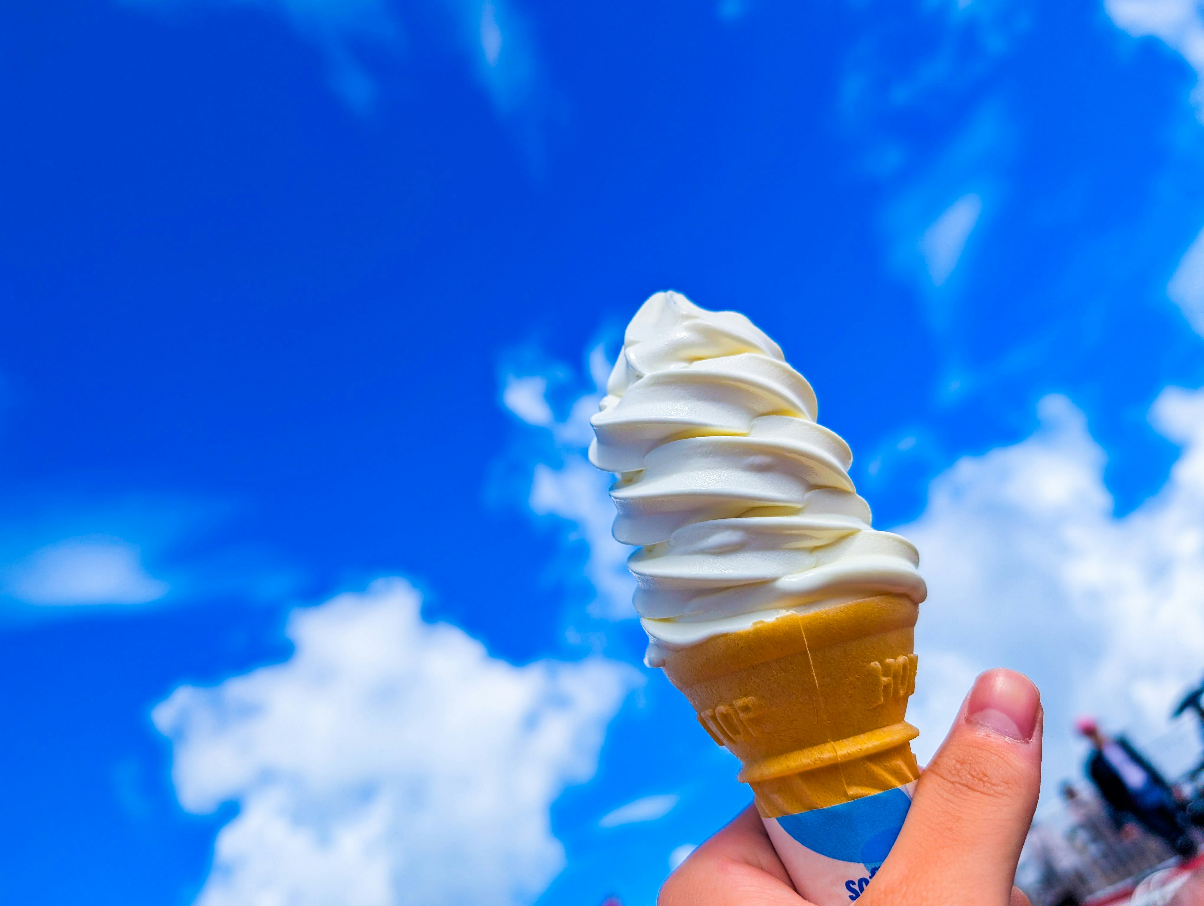 青空の下で手に持ったソフトクリーム