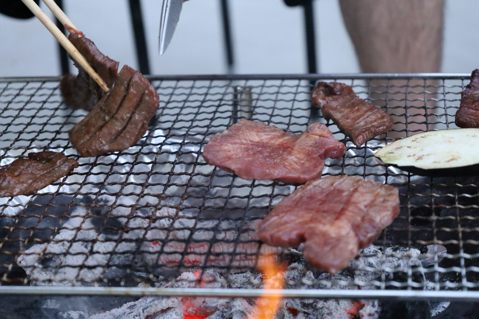 Fleischscheiben, die auf einem Grill braten mit Händen, die Essstäbchen halten