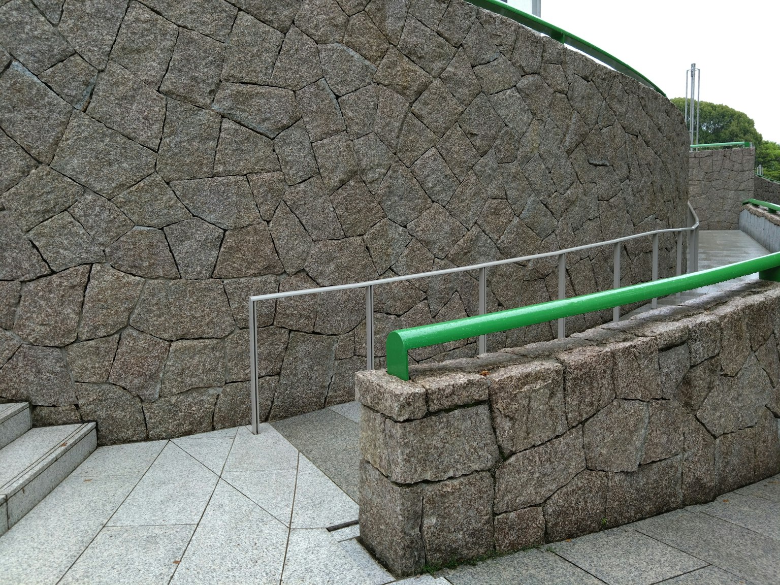 Glatter Steinmauer mit grünem Geländer auf einem Weg