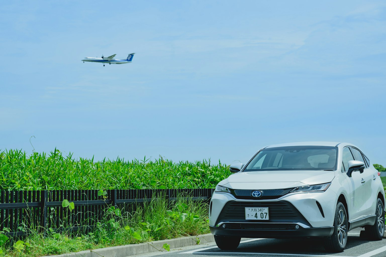 Un coche blanco estacionado al borde de la carretera con un avión volando en el cielo azul