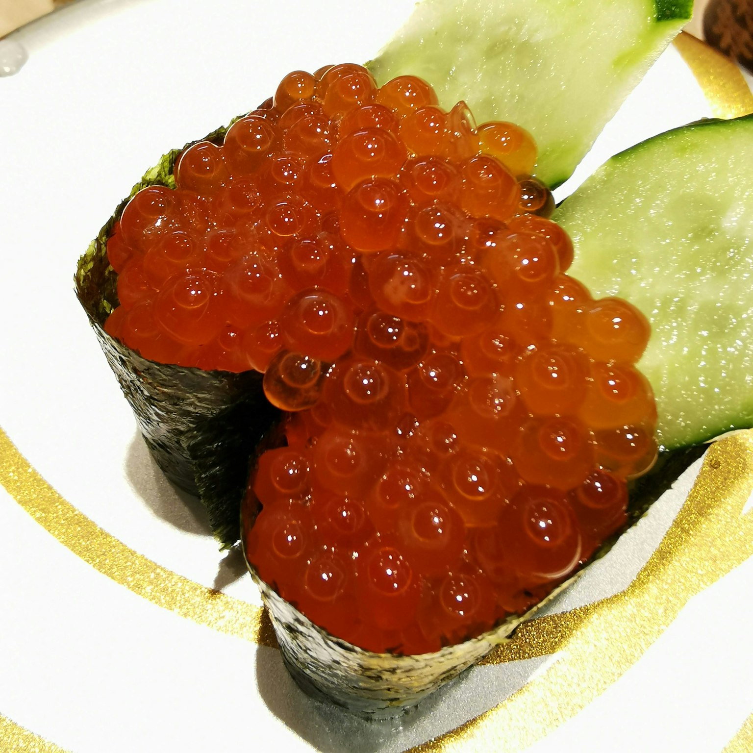 Un morceau de sushi garni de caviar de saumon vibrant accompagné d'algues et de concombre