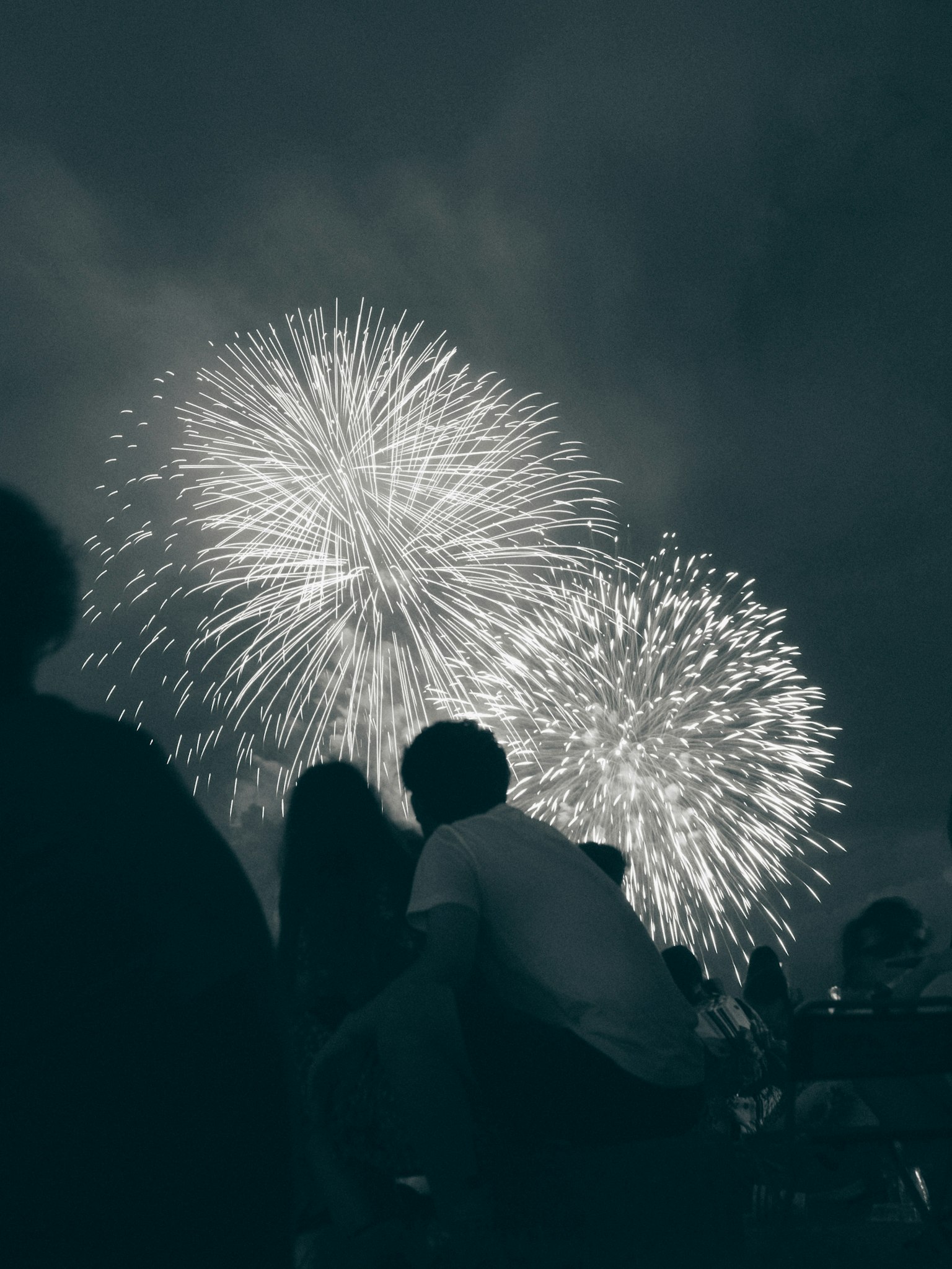 Fuochi d'artificio esplodono nel cielo notturno con sagome di persone che guardano