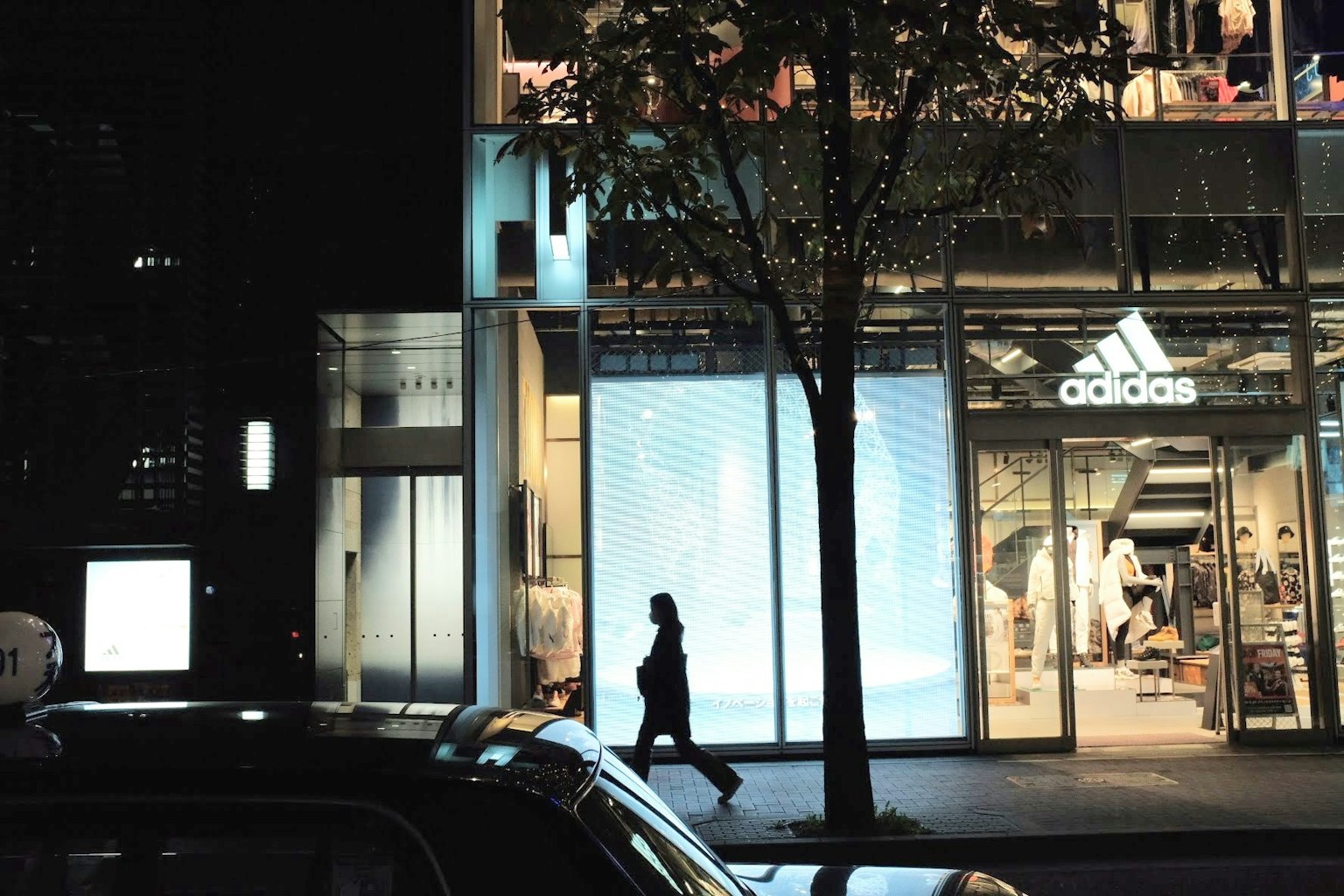 Orang berjalan di malam hari dengan toko Adidas terlihat