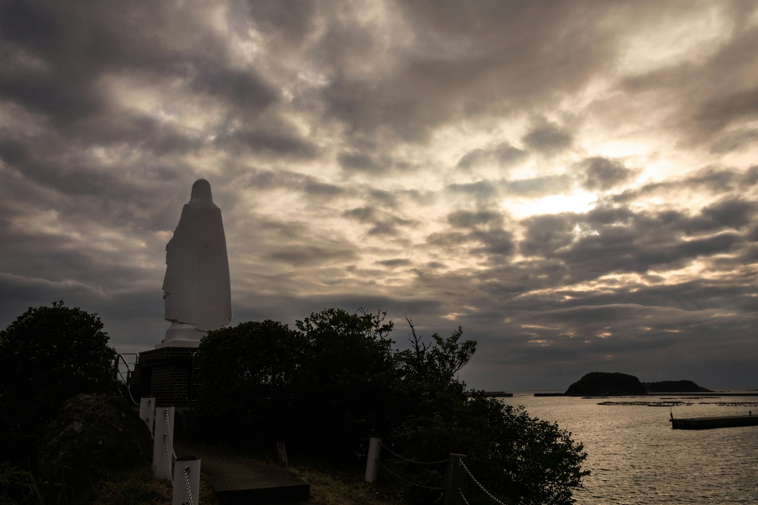 Statue blanche faisant face à la mer sous un ciel nuageux