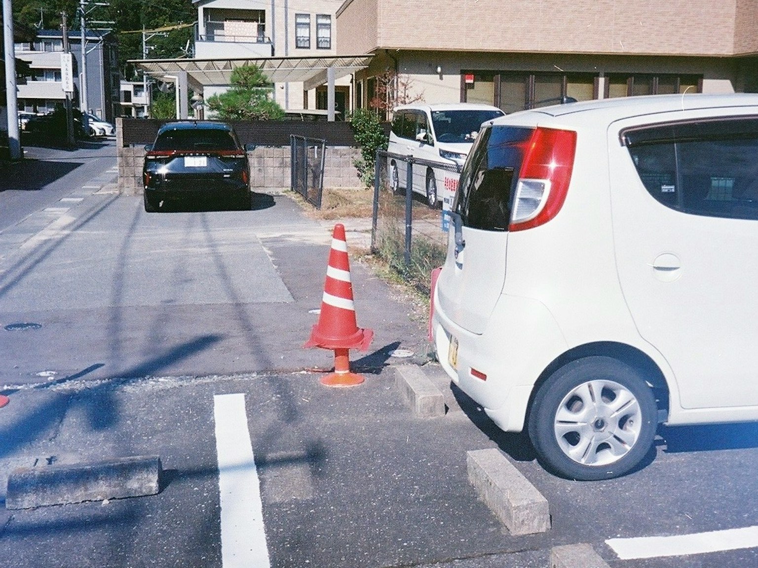白い車と黒い車が並ぶ道路の風景 赤いコーンが駐車スペースの近くに置かれている