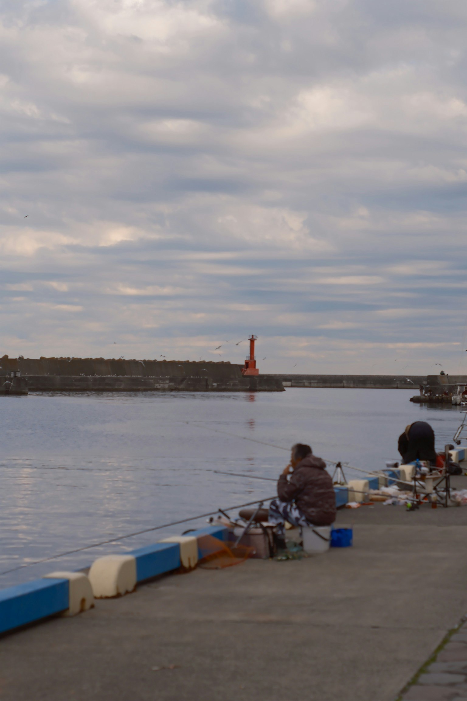 漁師が港で釣りをしている風景 赤い灯台が水面に映る