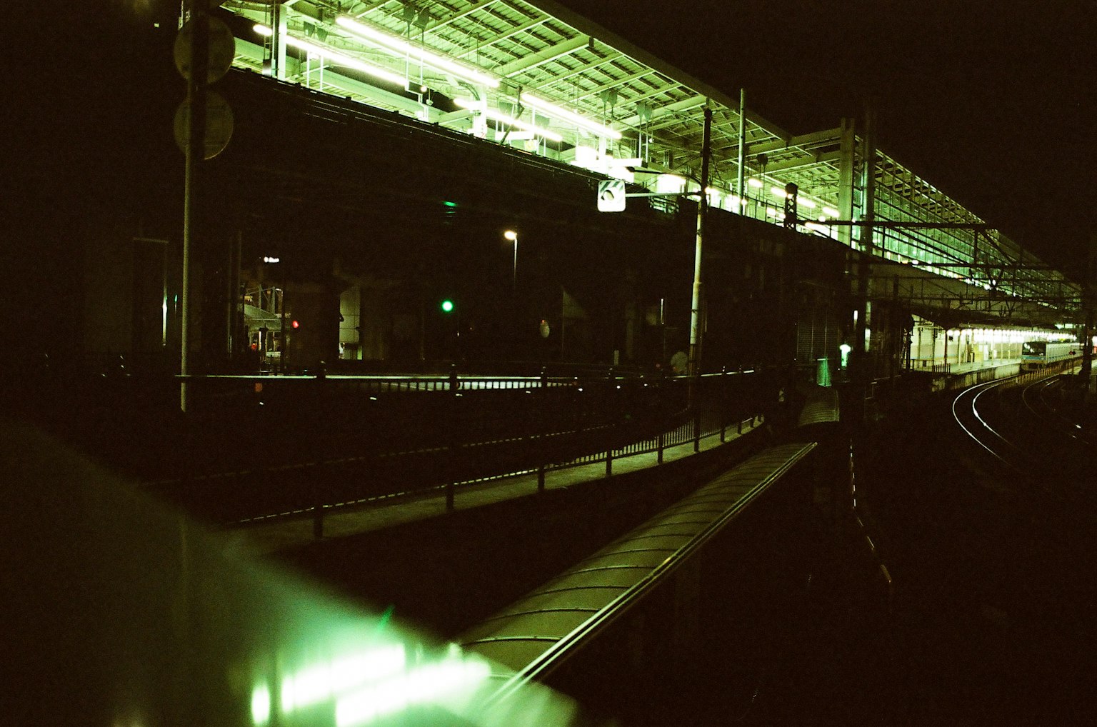 Nighttime railway station platform with vibrant green lighting and curved tracks
