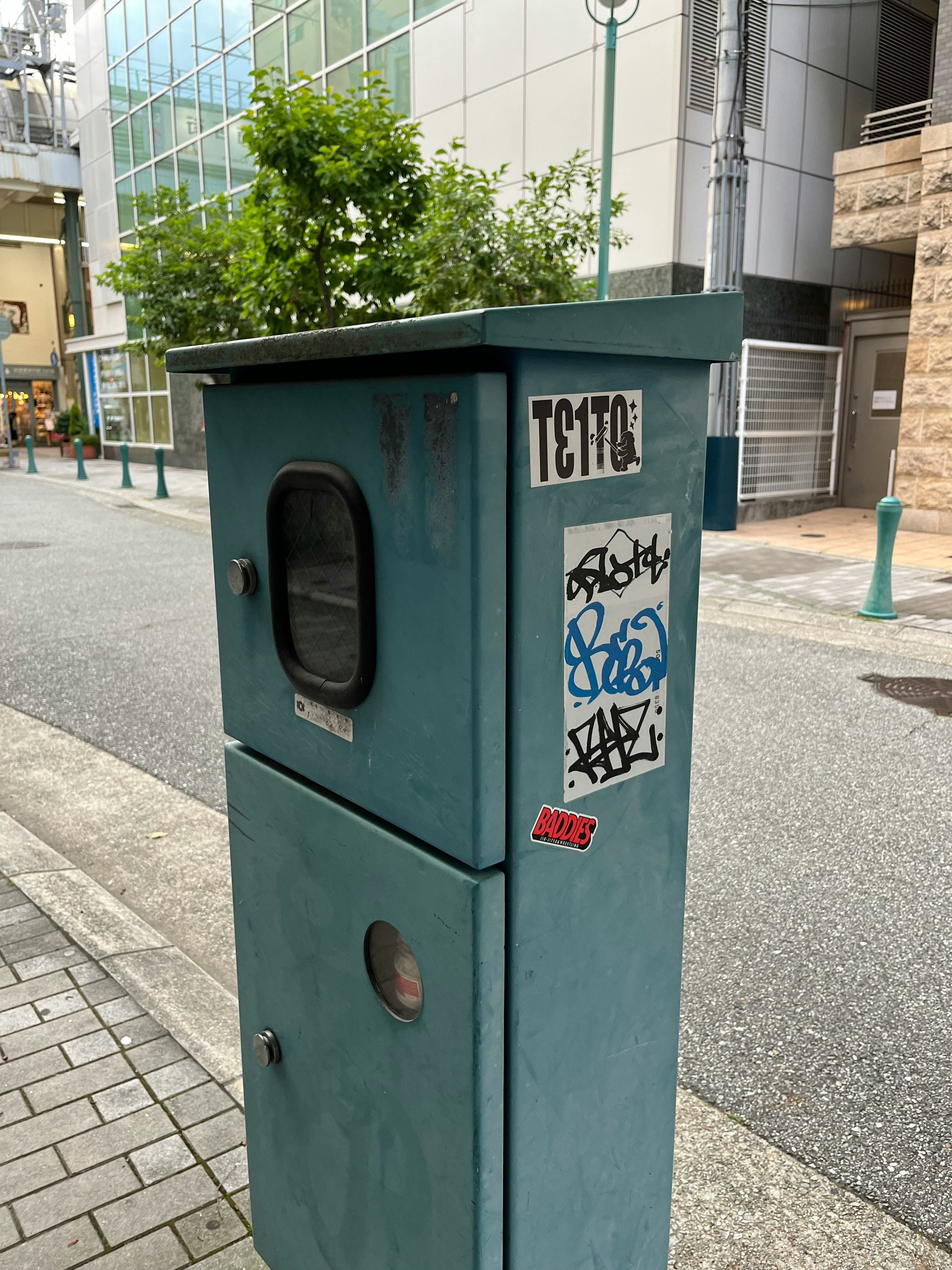 bidone della spazzatura verde con graffiti su un marciapiede urbano