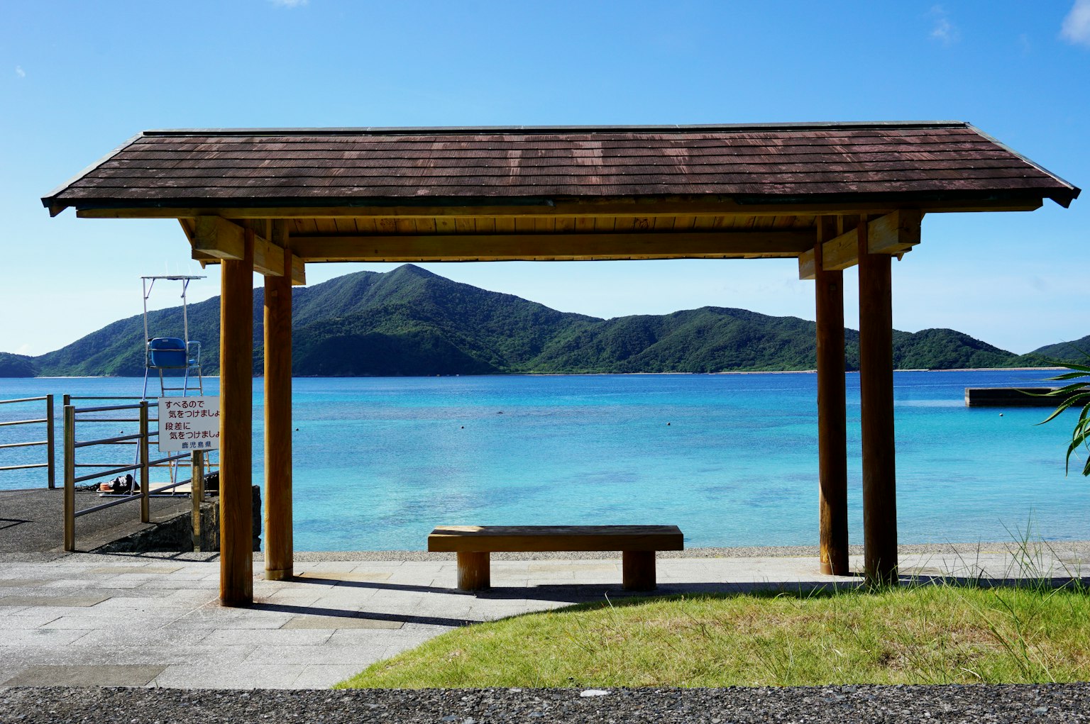 Beach pavilion with wooden bench overlooking blue sea and mountains