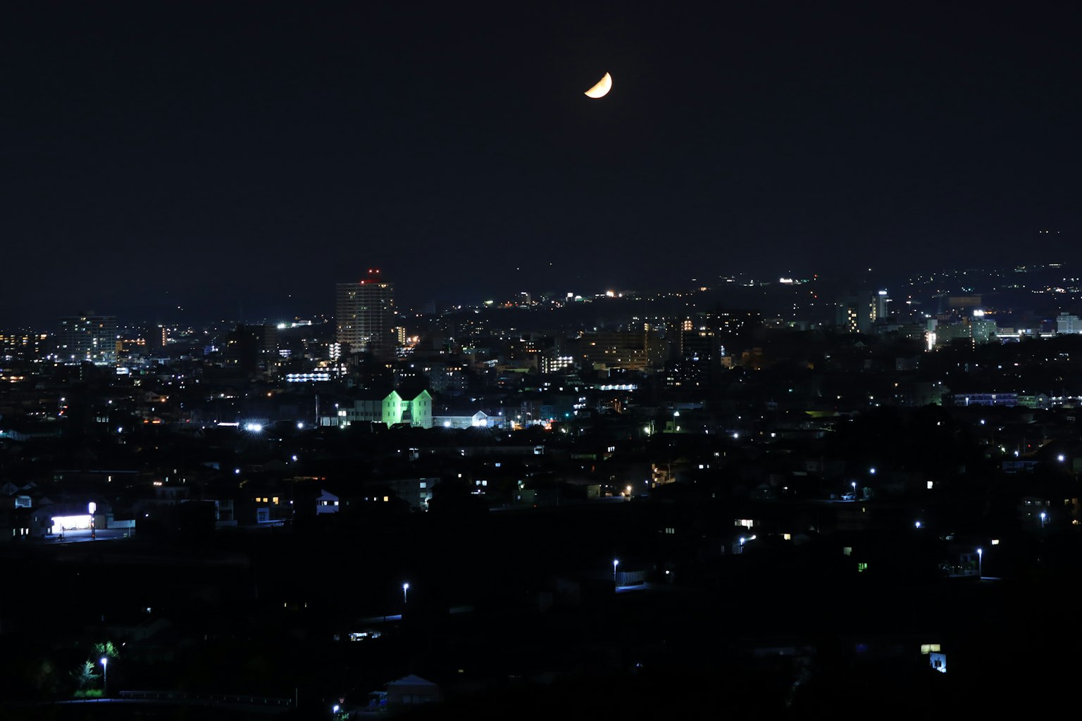 Nachtsicht auf die Skyline einer Stadt mit einem Mond und beleuchteten Gebäuden