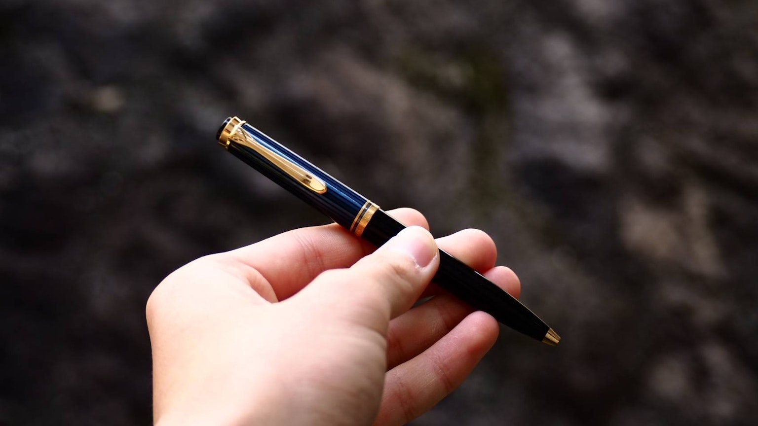 Una mano che tiene una penna stilografica blu di lusso con accenti dorati