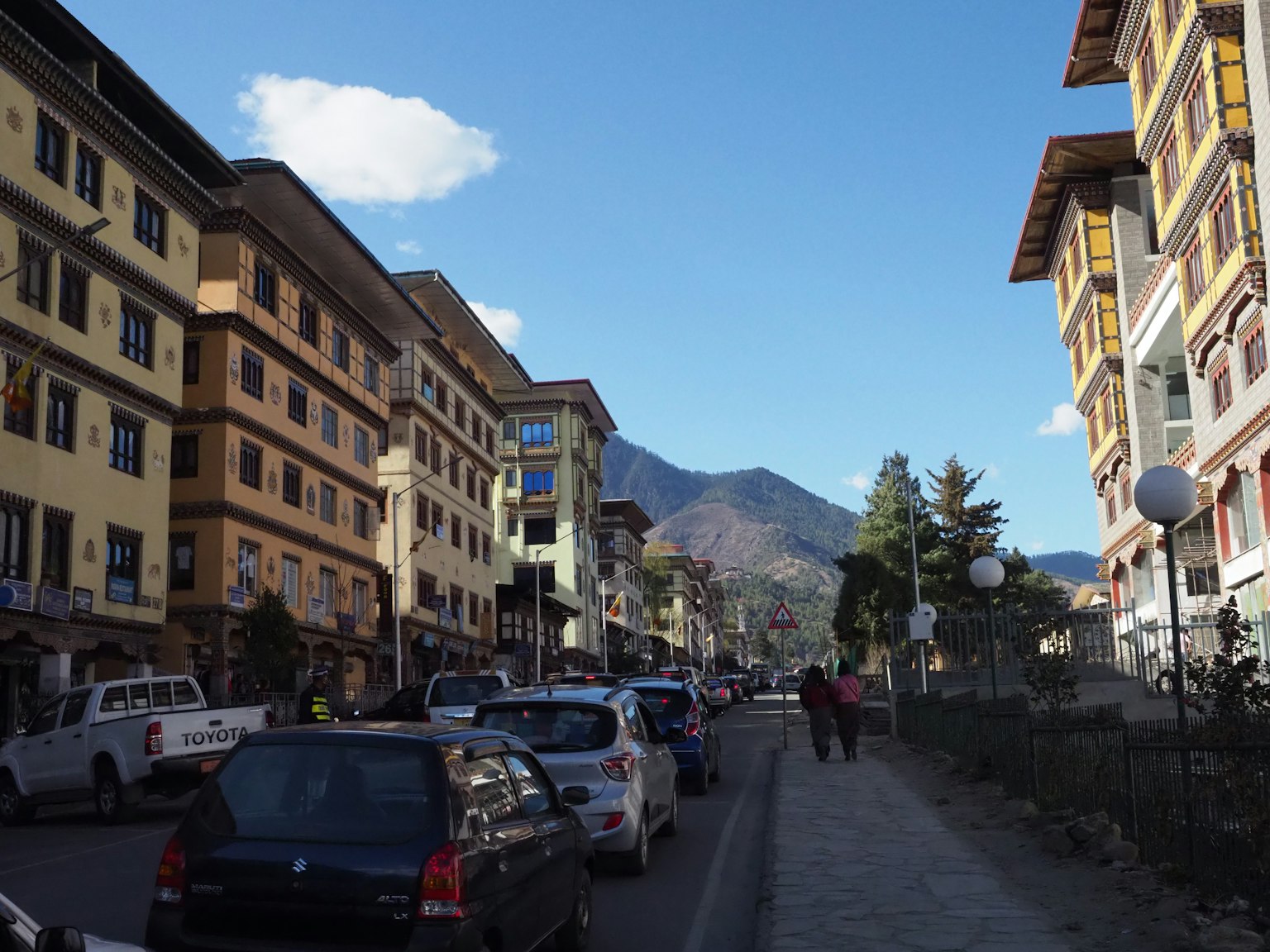 Paysage urbain du Bhoutan avec une rue bordée de bâtiments et de voitures garées montagnes pittoresques en arrière-plan
