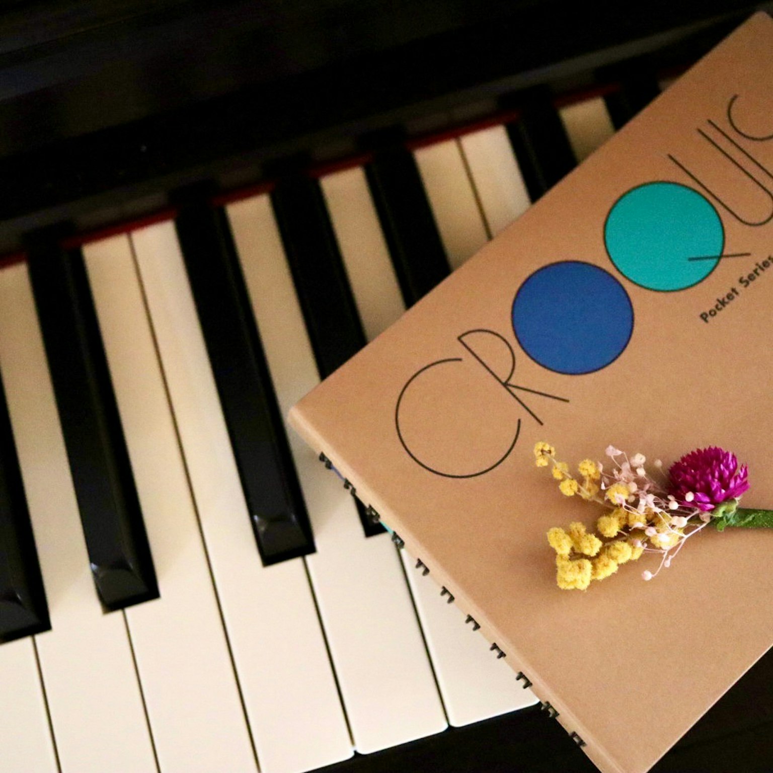 Carnet de croquis intitulé Croquis posé sur des touches de piano avec des fleurs colorées