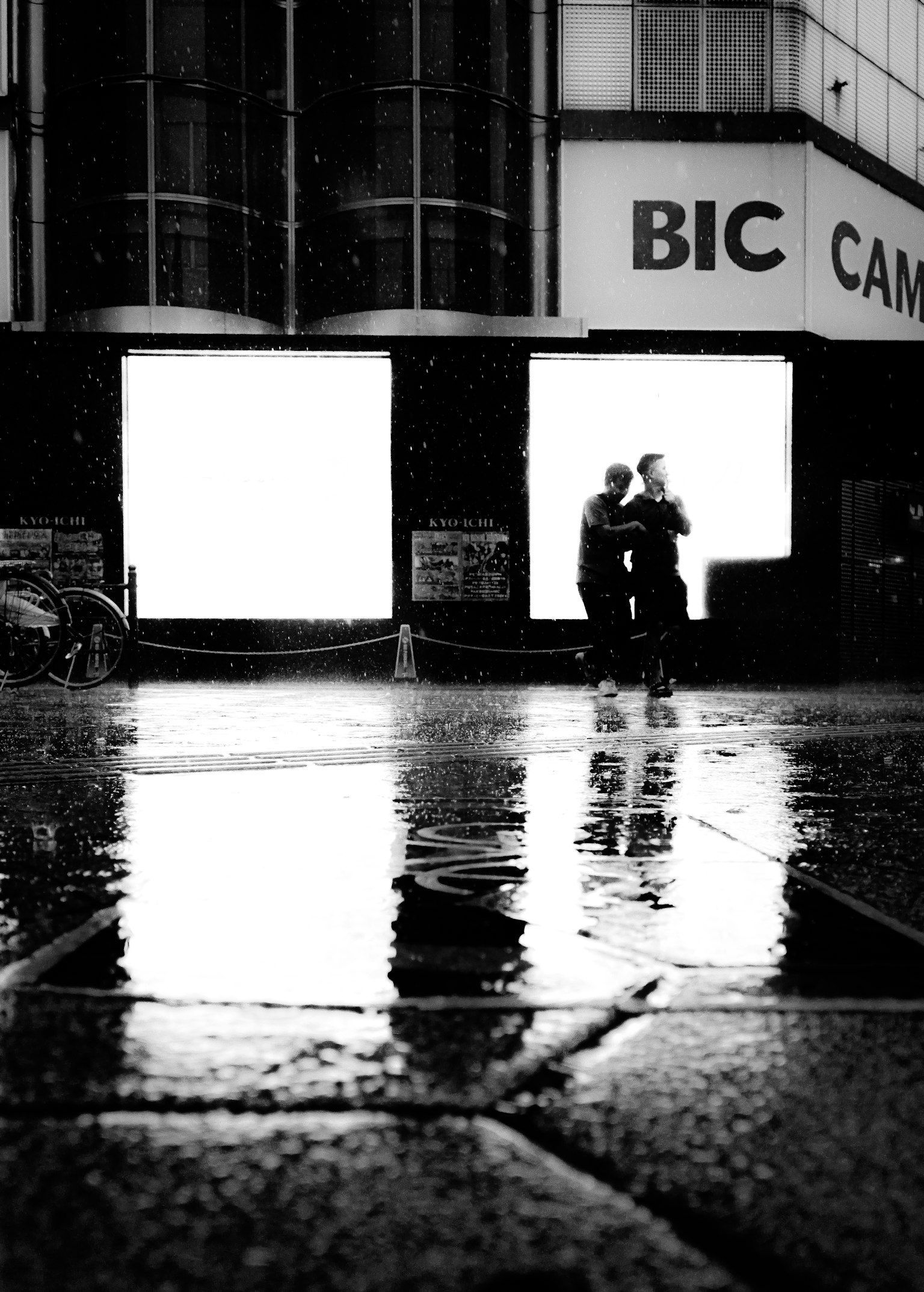 Black and white photo of a couple embracing in the rain with reflections in puddles