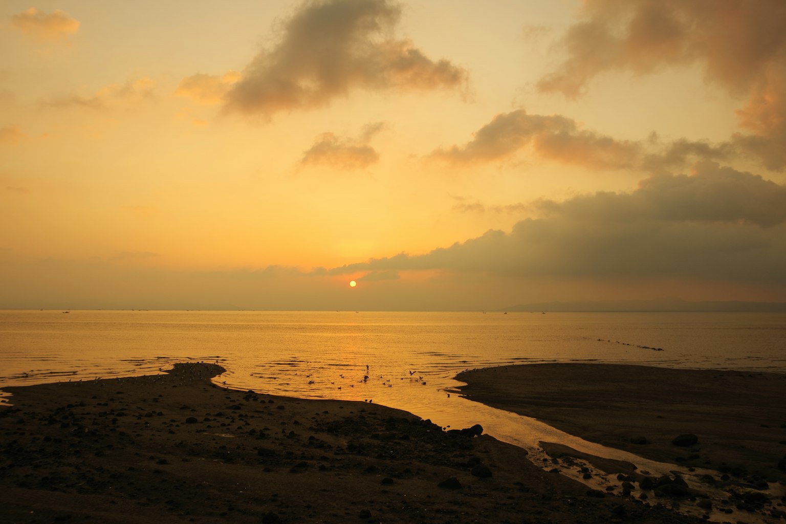 Matahari terbenam di lautan dengan langit oranye dan kuning yang cerah pemandangan pantai pasir dan bebatuan