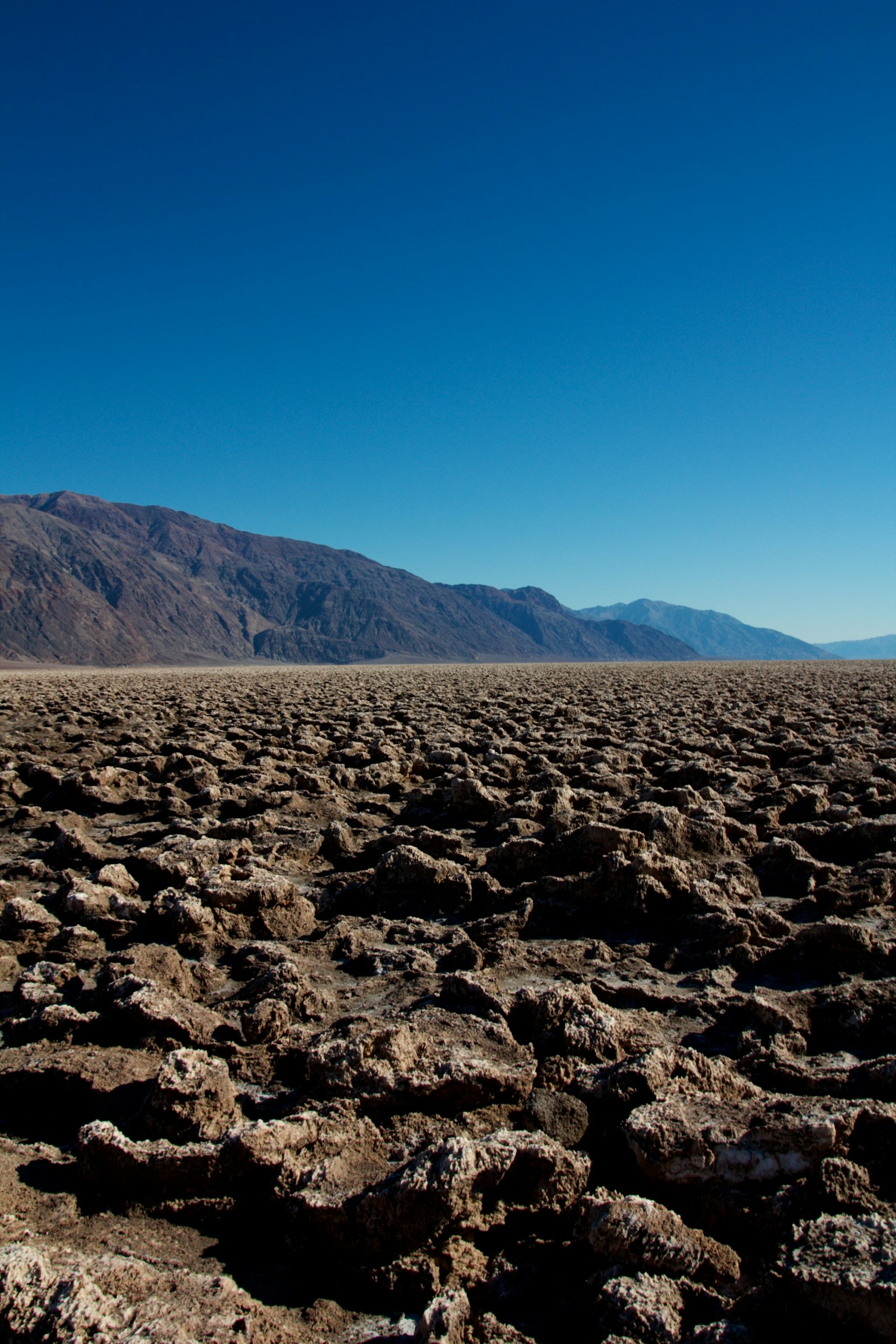 Paesaggio desolato della Death Valley con terra crepata e cielo blu chiaro