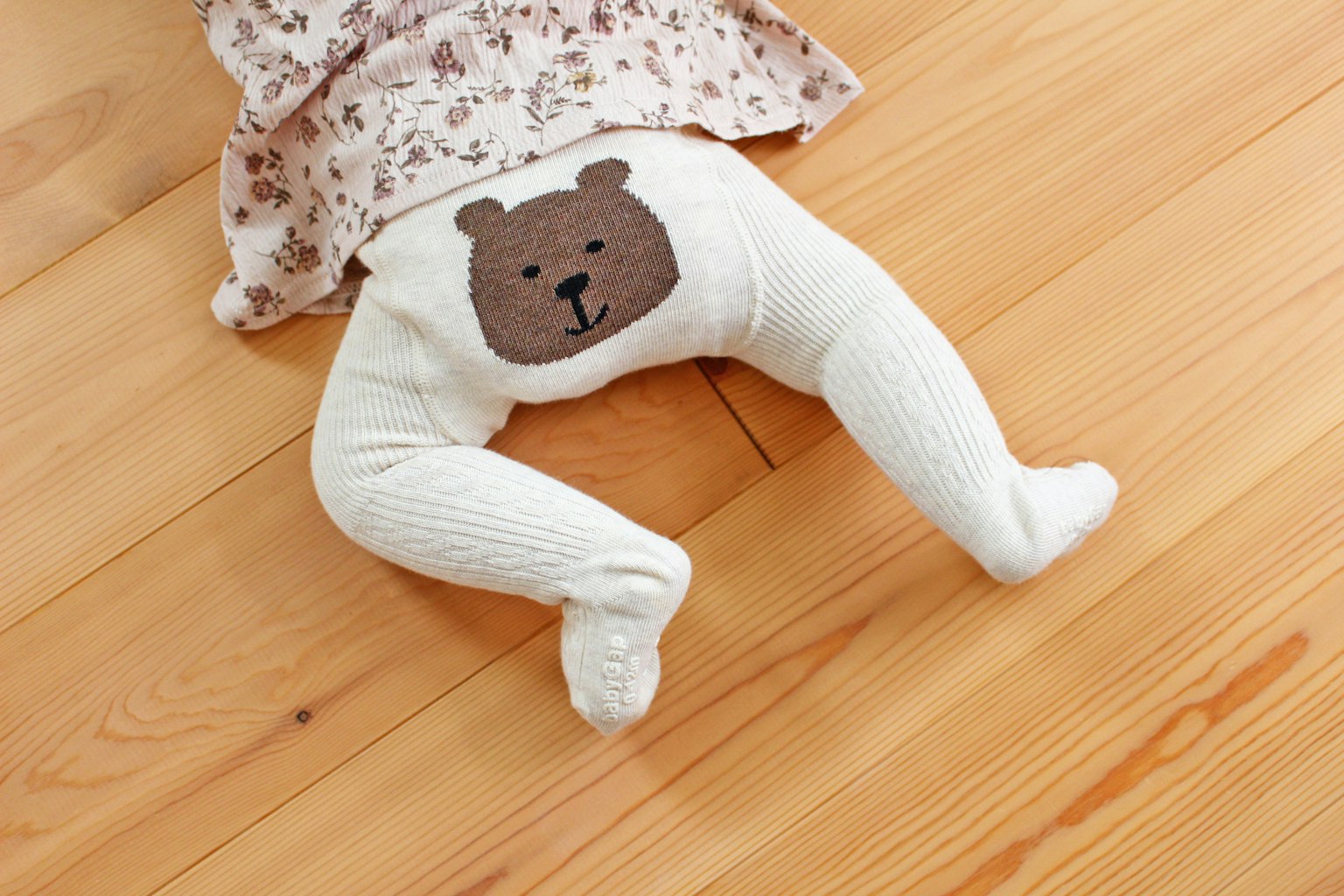아기가 뒤에 곰 얼굴 디자인이 있는 흰색 레깅스를 입고 있다