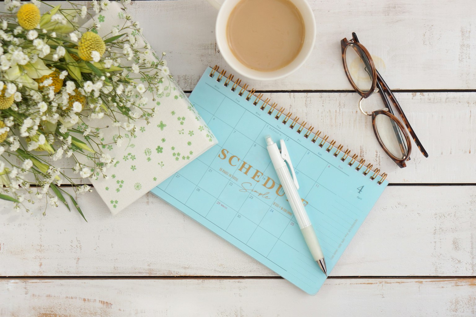 Quaderno blu e penna con tazza di caffè occhiali e bouquet su un tavolo