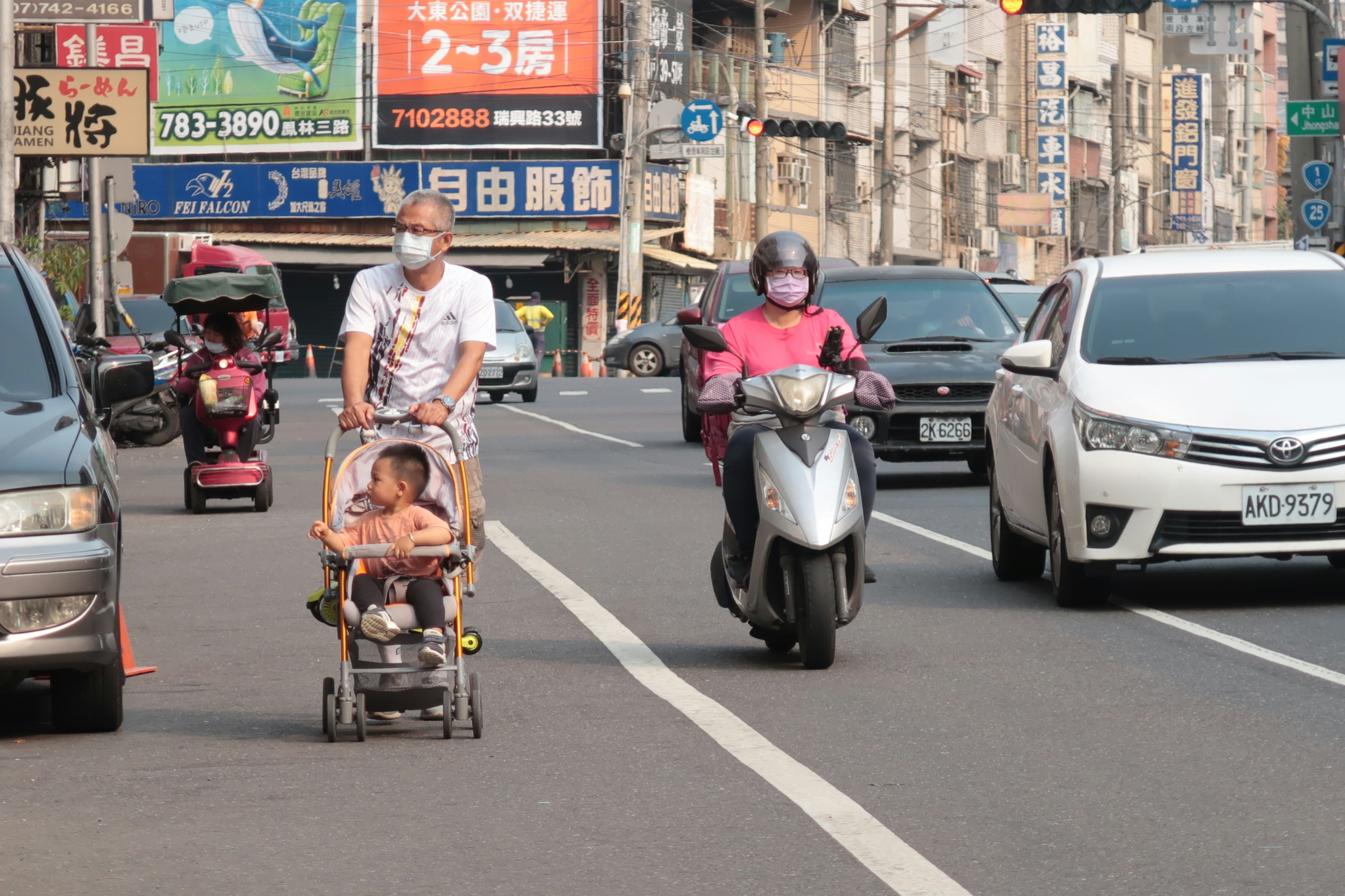 Scooter e passeggino in movimento su una strada di quartiere commerciale