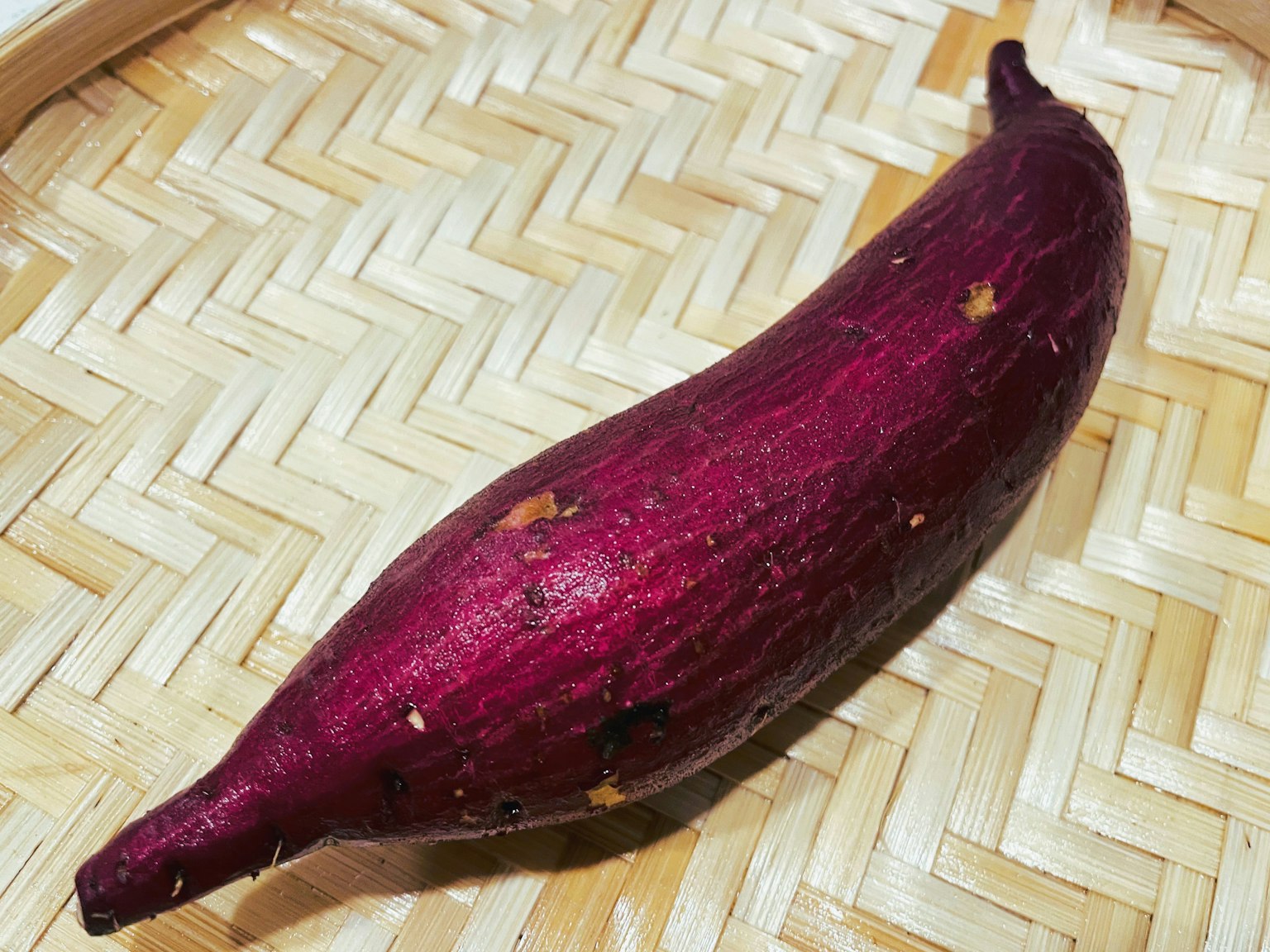 Una patata dolce viola posata su un cesto di bambù