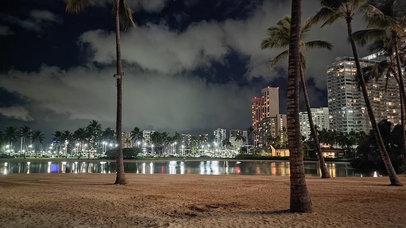 Nighttime view of Waikiki Beach featuring illuminated buildings and reflective water