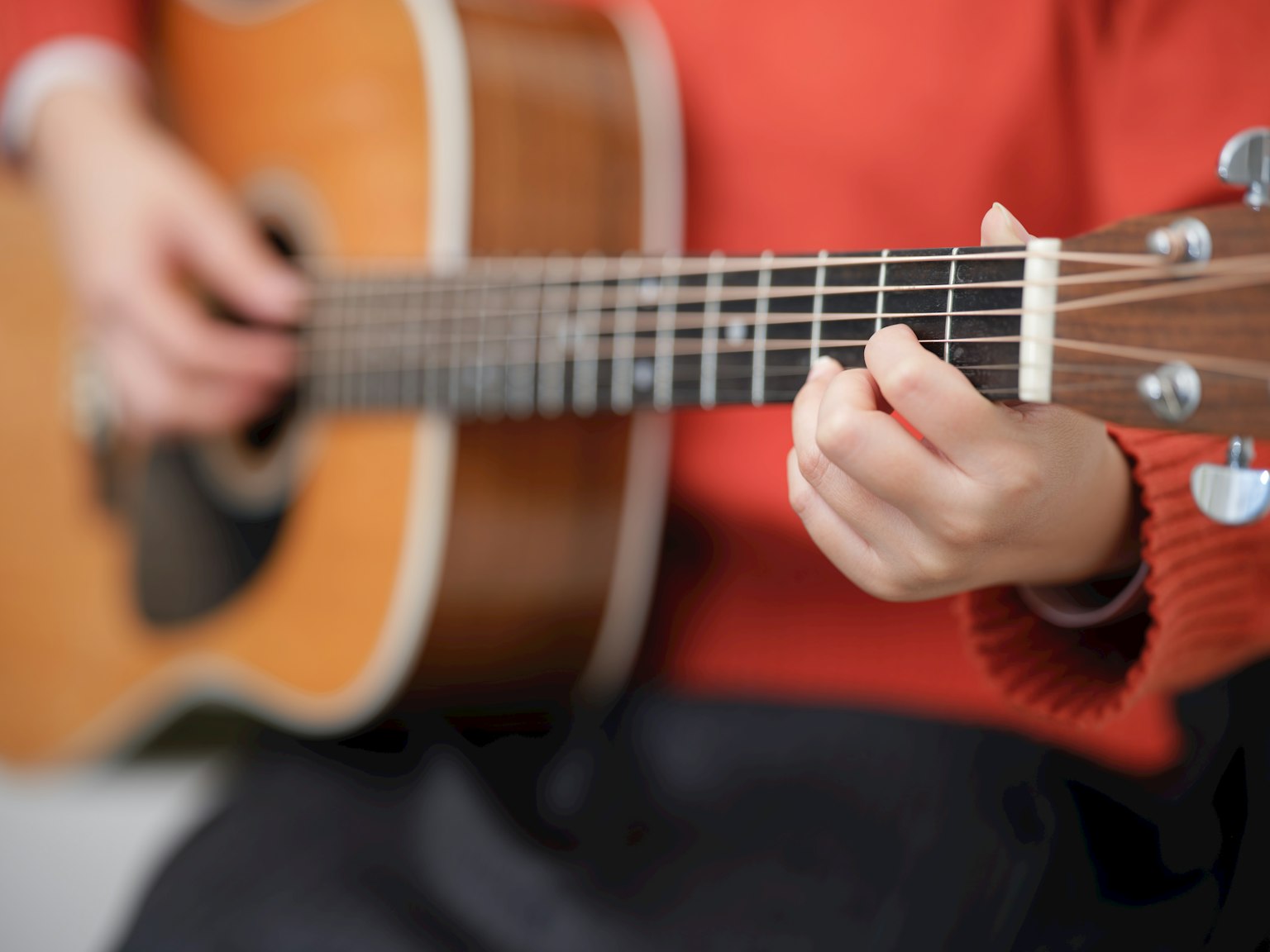 Gros plan sur des mains jouant une guitare acoustique personne portant un pull rouge