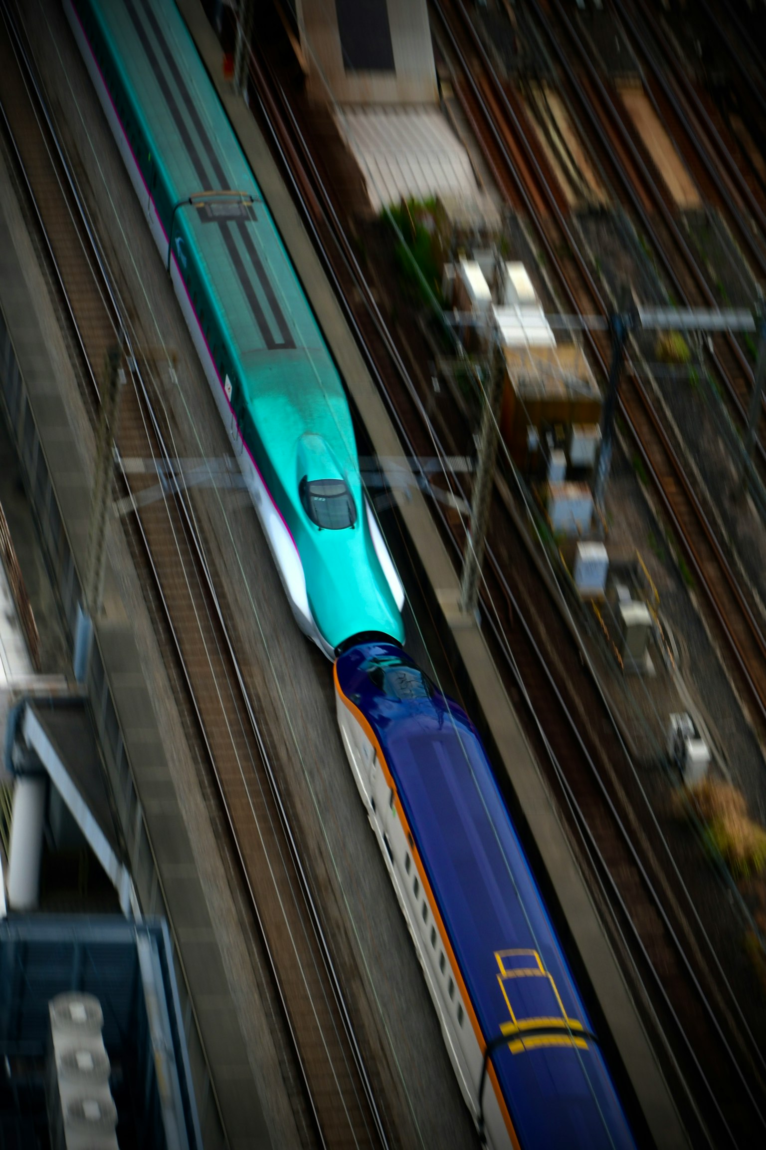 Luftaufnahme eines grünen Shinkansen und eines blauen Zuges, die sich auf Schienen kreuzen