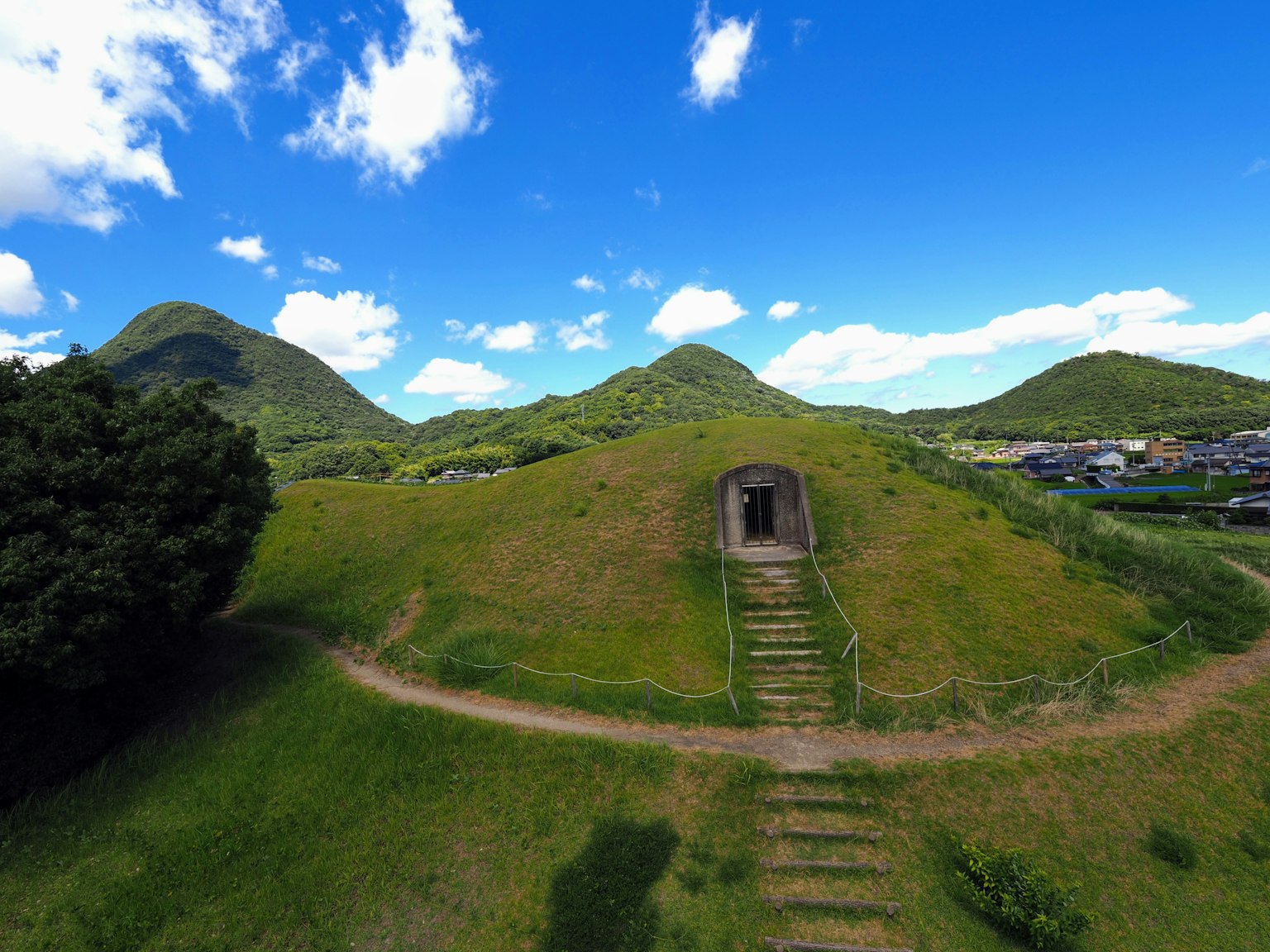 Entrada de un túmulo antiguo bajo colinas verdes y cielo azul