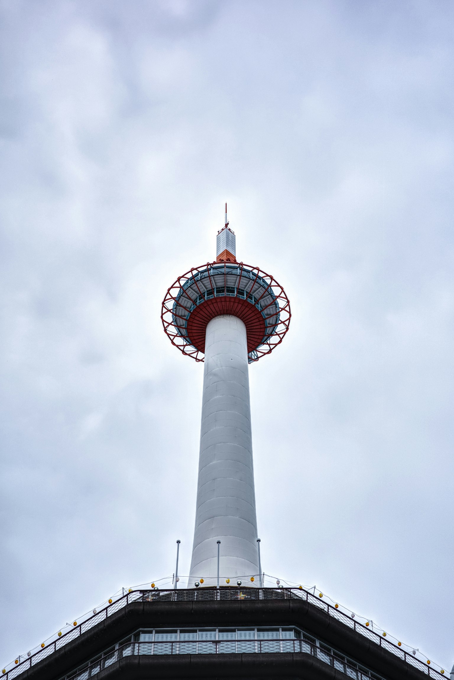 Vista de una torre alta desde abajo que se eleva hacia el cielo con una estructura blanca y un anillo rojo