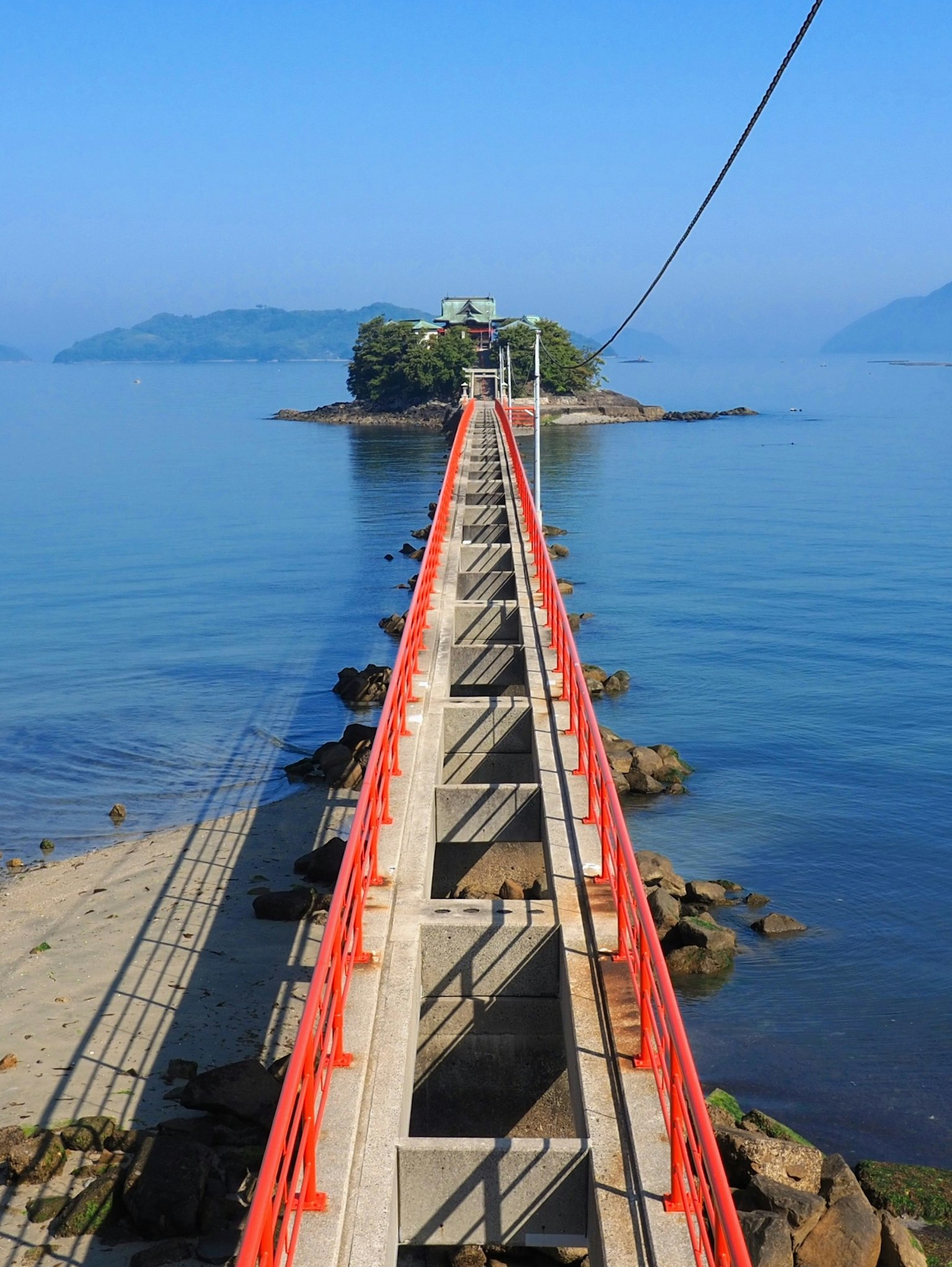 Rote Brücke, die über ruhige blaue Gewässer zu einer kleinen Insel führt