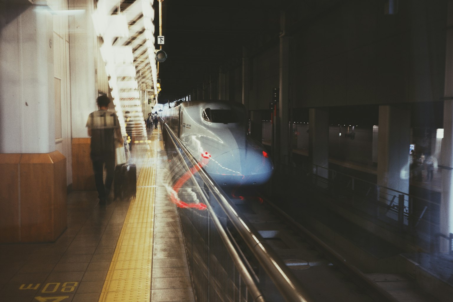 Un tren pasando por una estación de noche con una figura borrosa