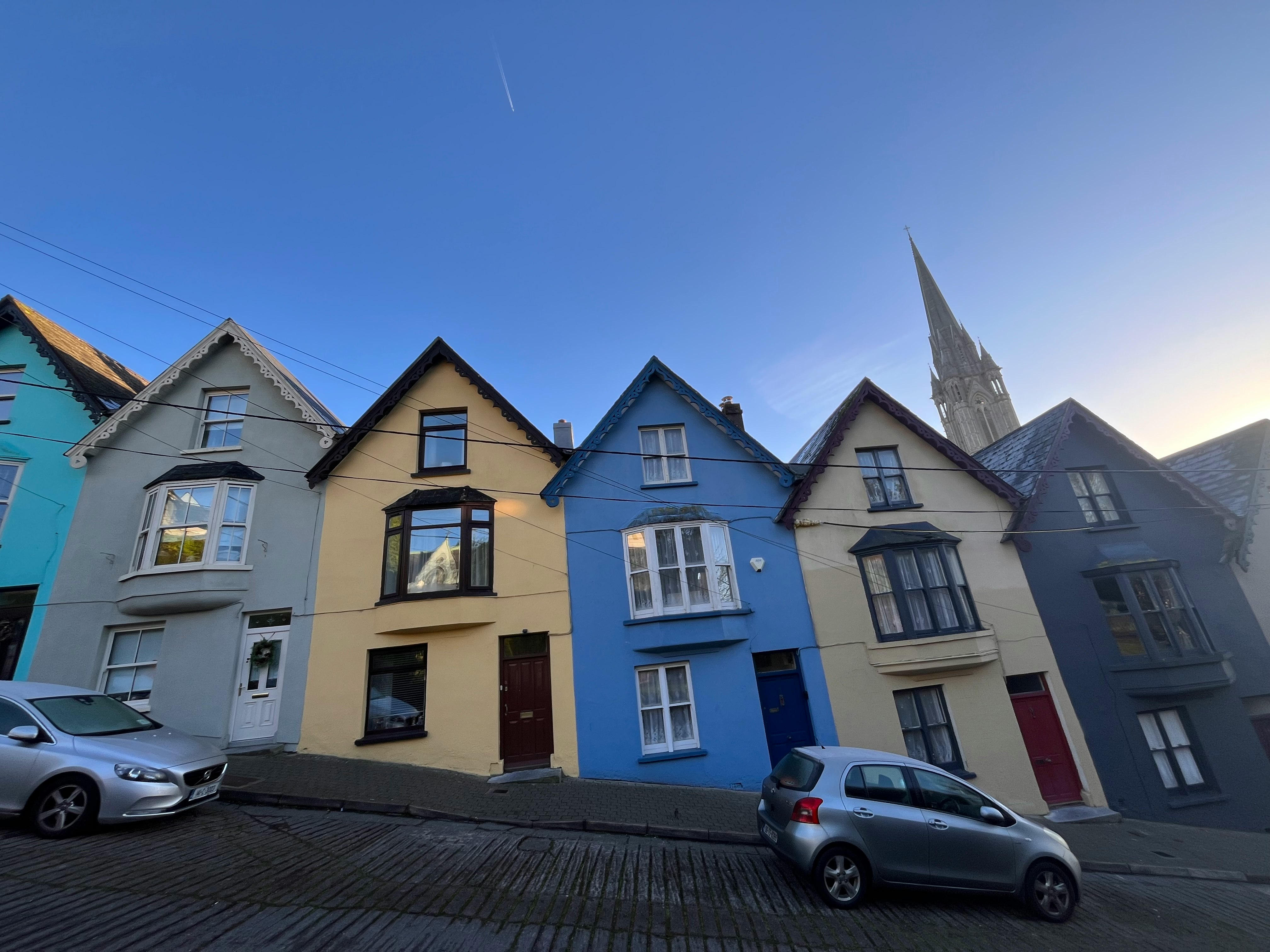 colorful row houses and parked cars on a street under a blue sky
