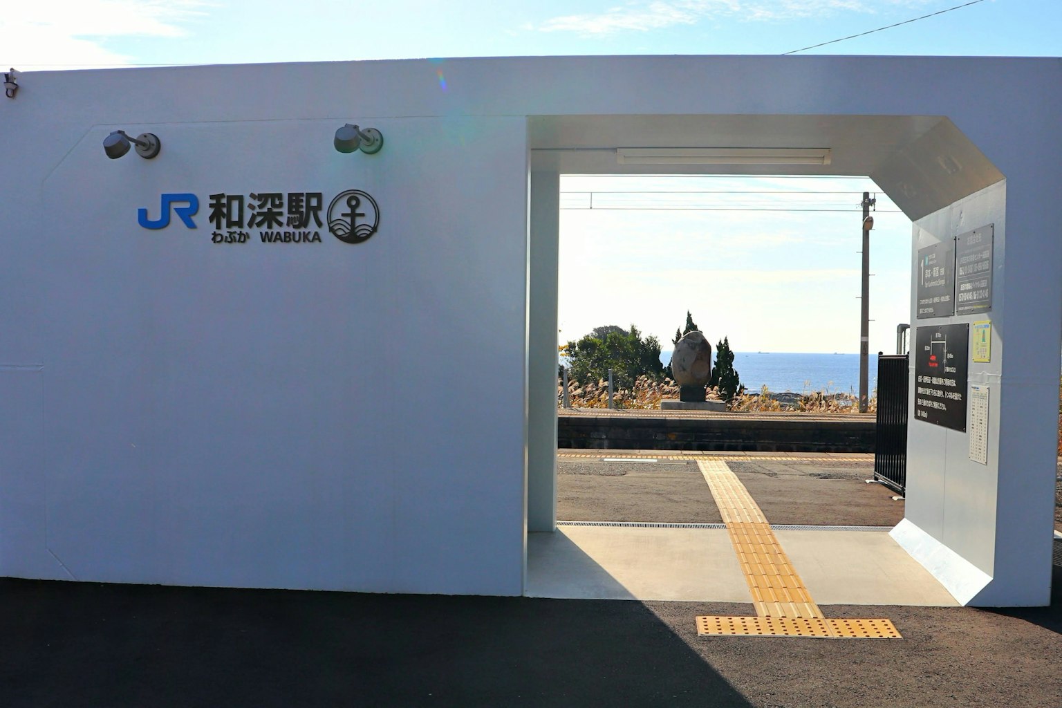 Entrée de la gare JR de Wakayama avec des murs blancs et vue sur l'océan