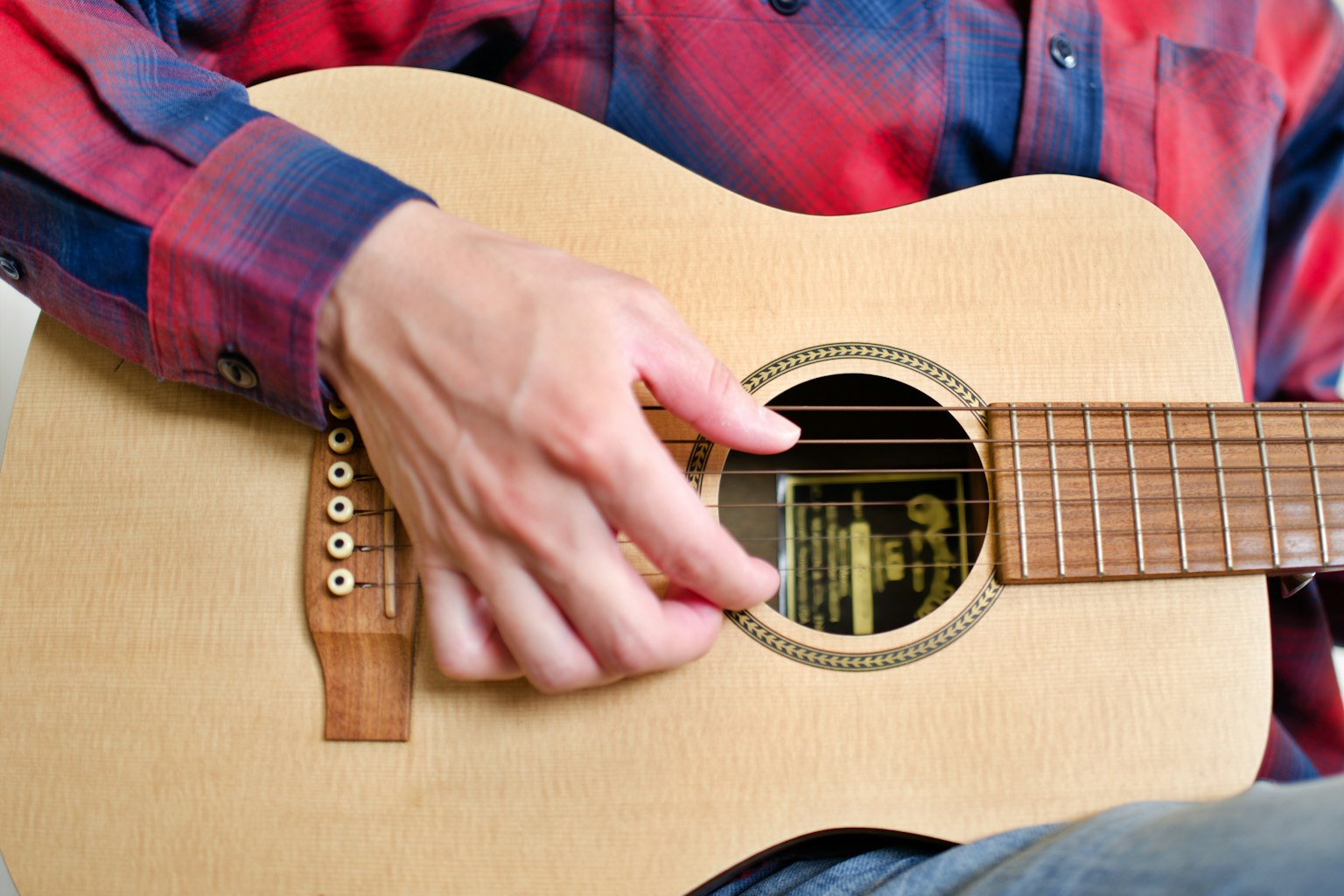 Kedekatan tangan yang memainkan gitar dengan kemeja kotak-kotak