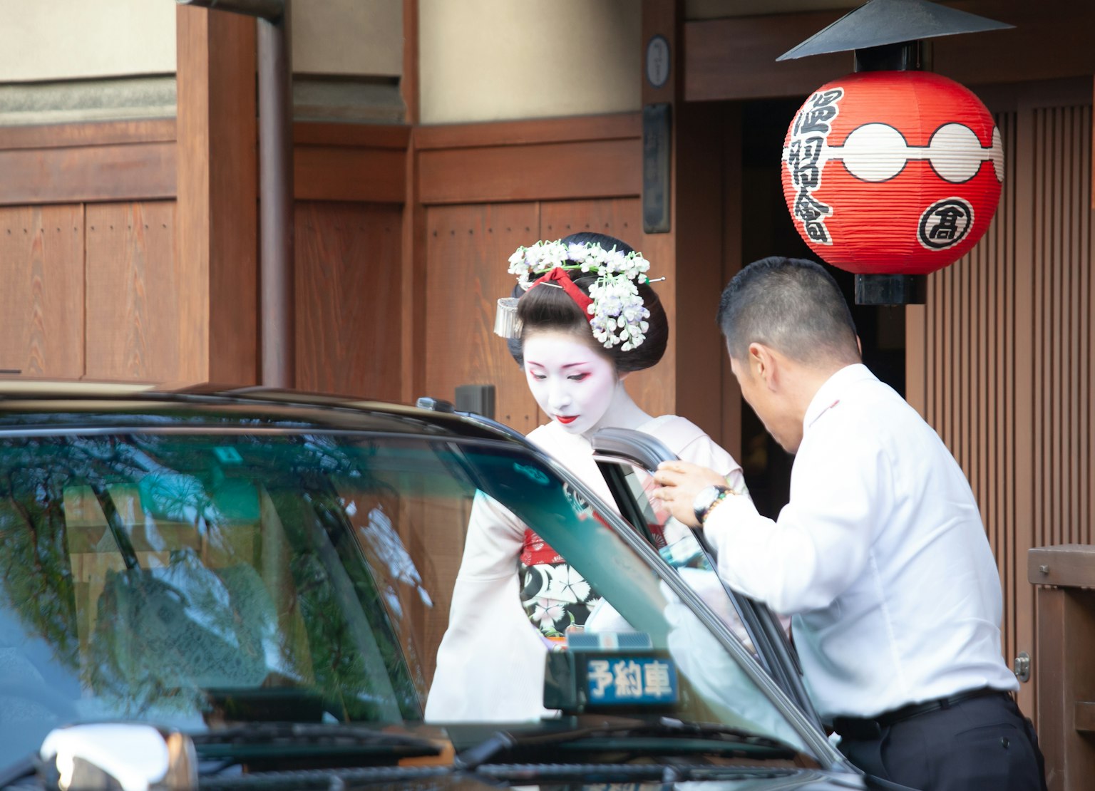 Một geisha trong kimono truyền thống đang được một người đàn ông giúp ra khỏi xe