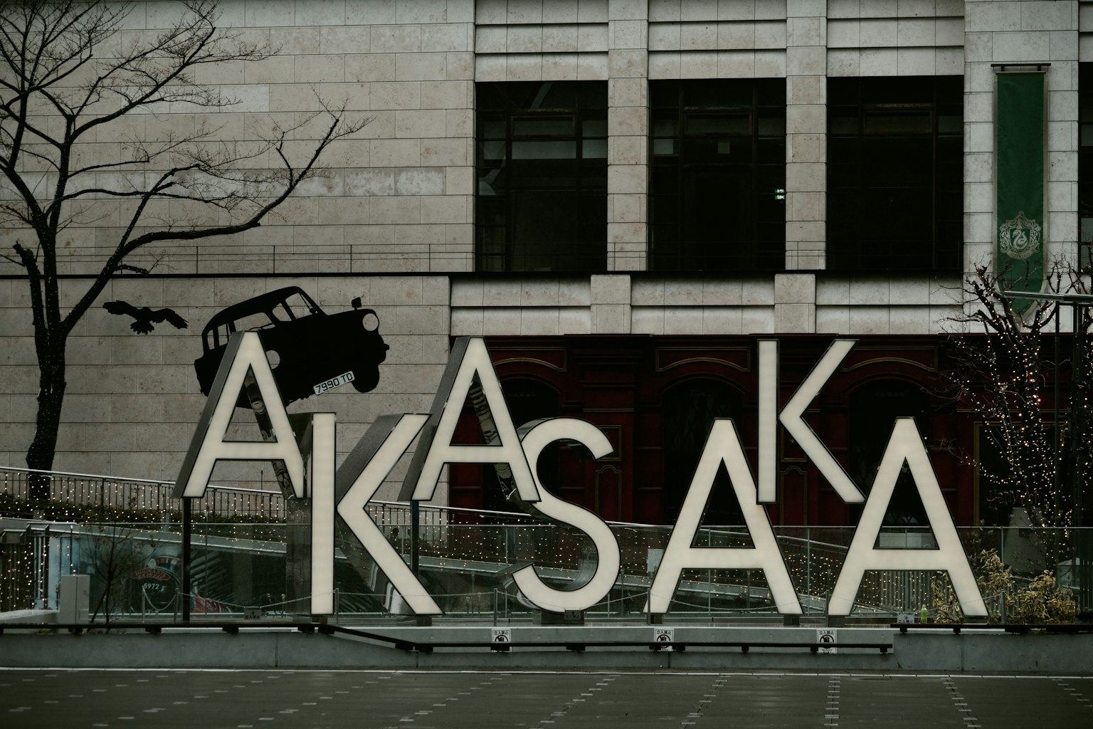 Kunstinstallation mit großen Buchstaben, die 'AKASAKA' buchstabieren, und einem Baumzweig mit der Silhouette eines Autos im Hintergrund