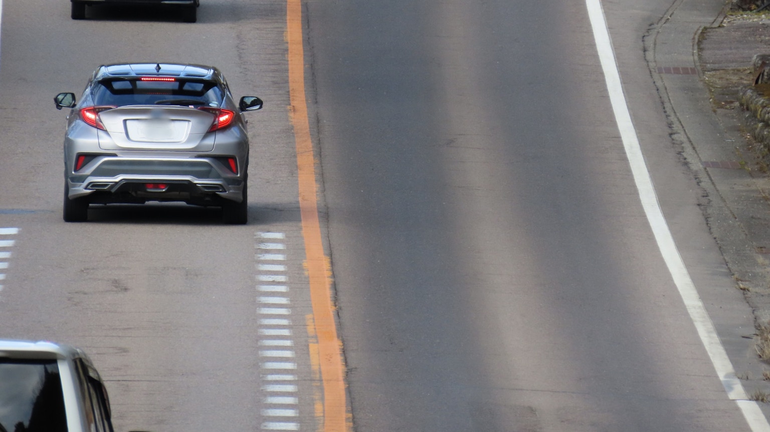 Silver car driving on highway with orange lane markings