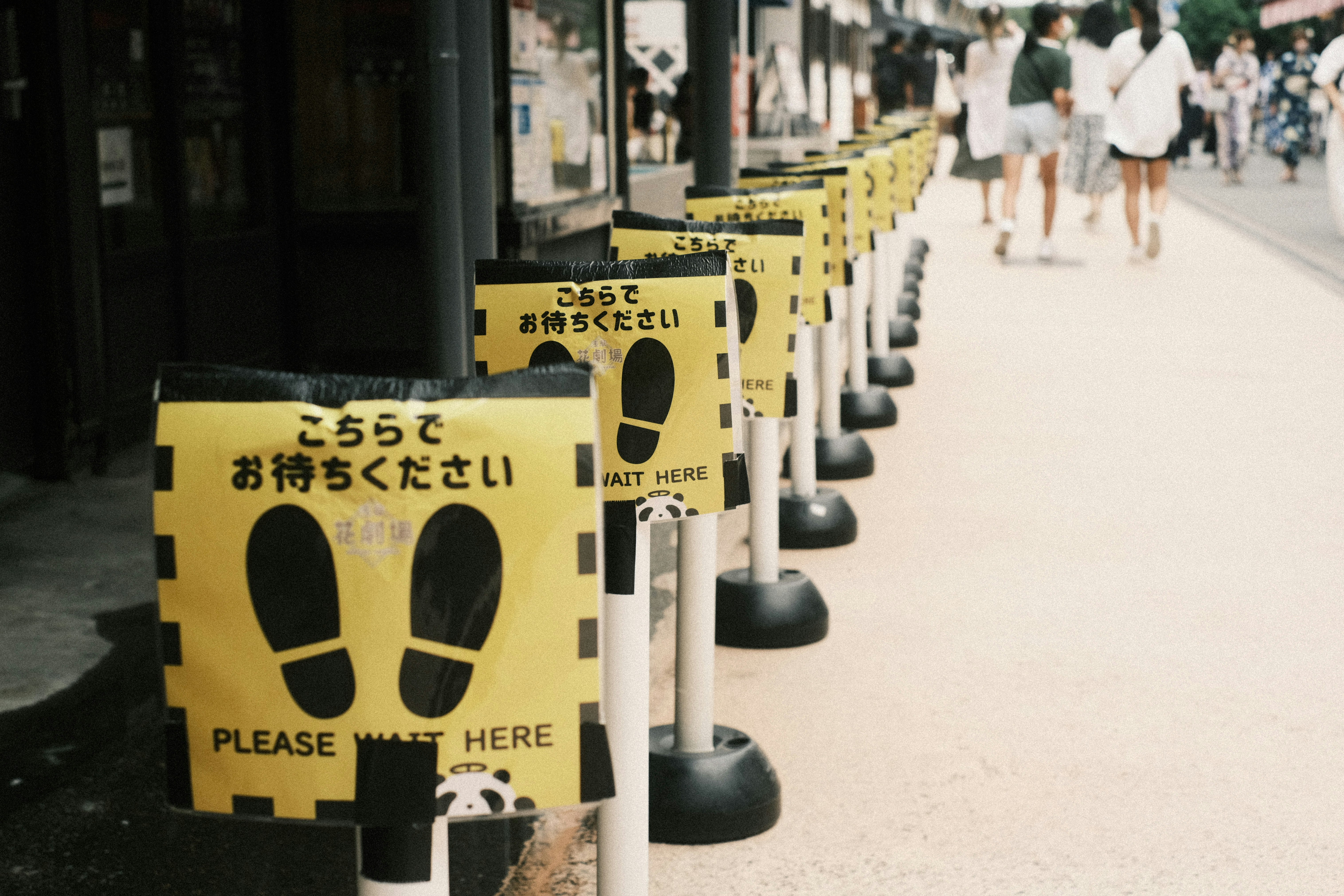 Yellow queue guidance tape and a row of black stanchions along a shopping street