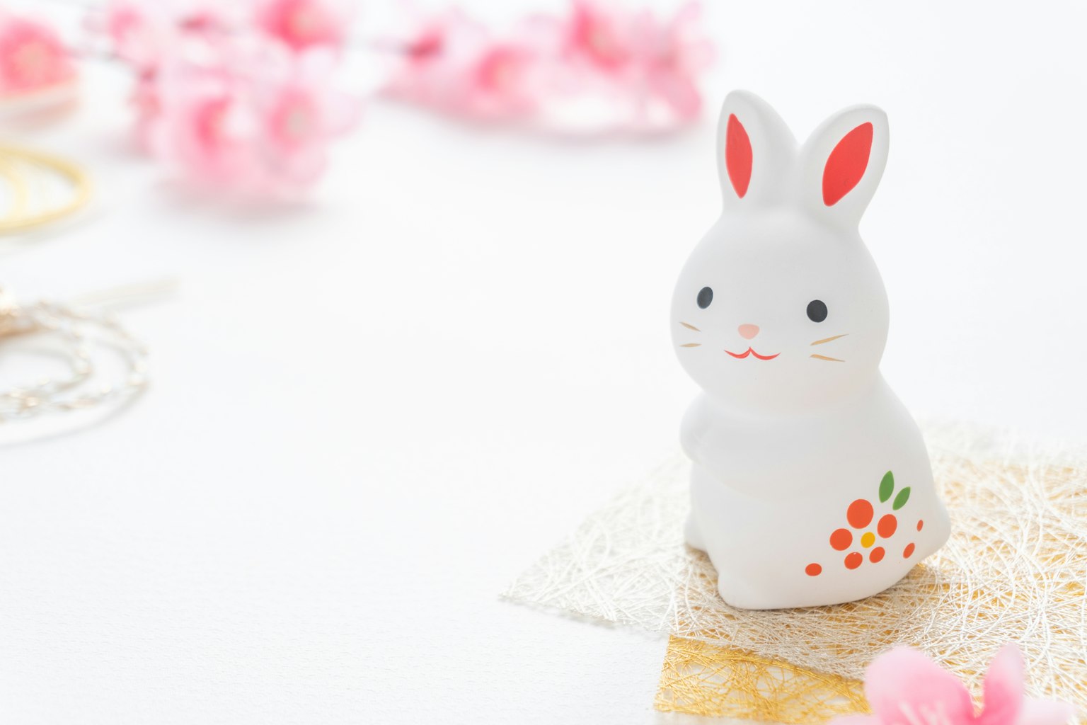 ตุ๊กตากระต่ายสีขาวมีลวดลายสีส้มวางอยู่บนพื้นหลังของดอกไม้สีชมพู